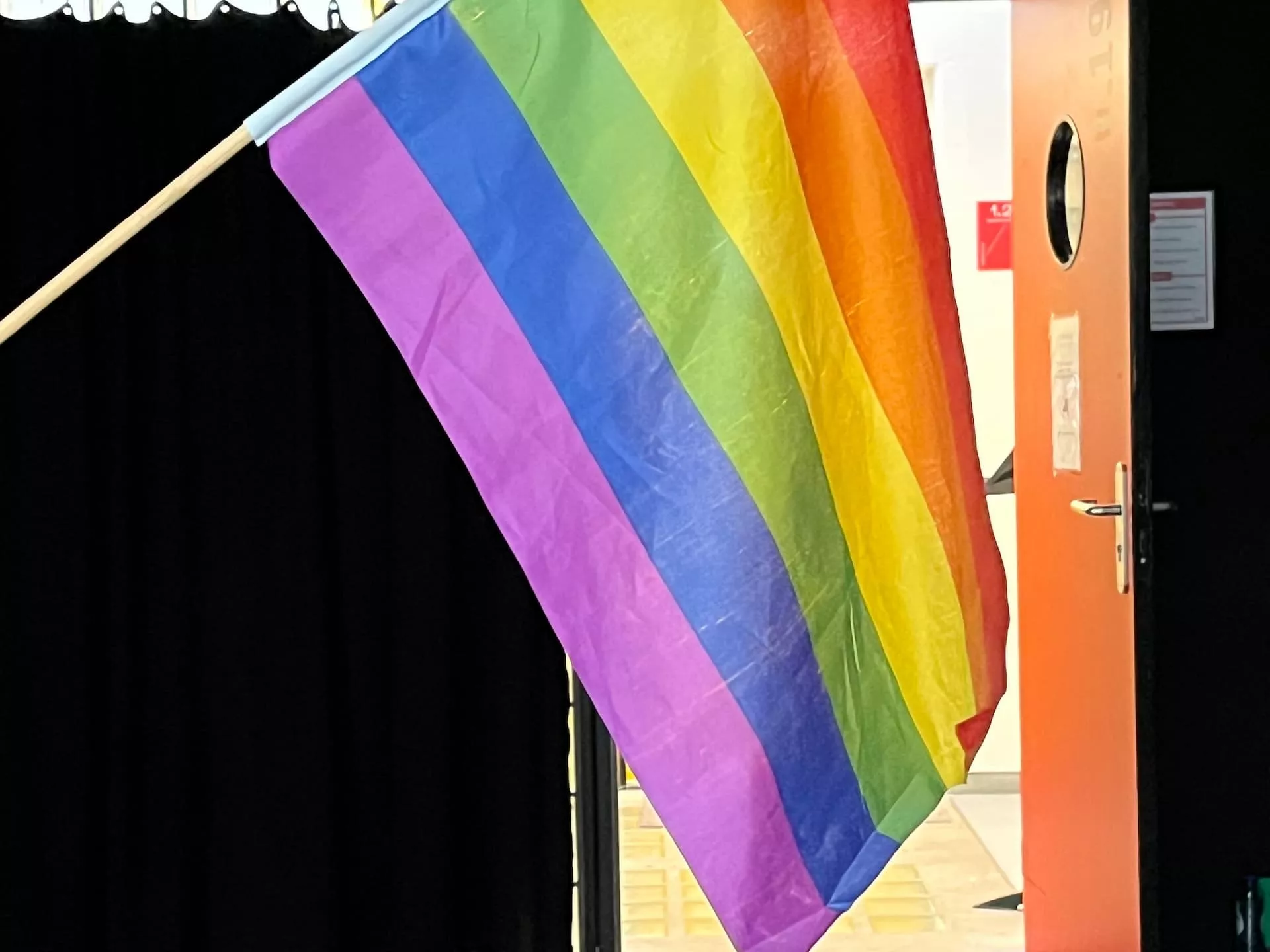 Regenboogvlag bij een open deur in een donkere ruimte.