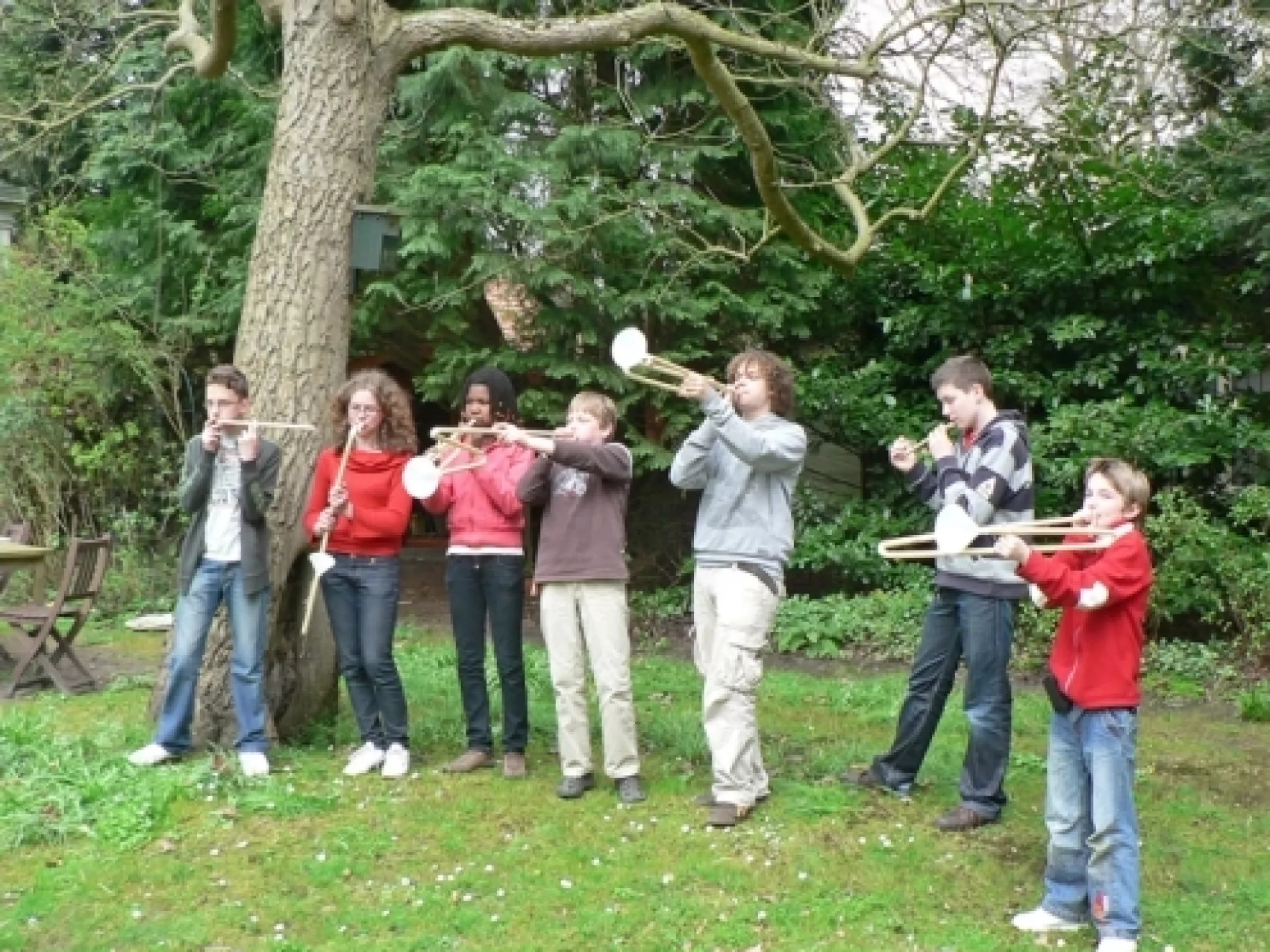 Groep kinderen met zelfgemaakte instrumenten bij een boom