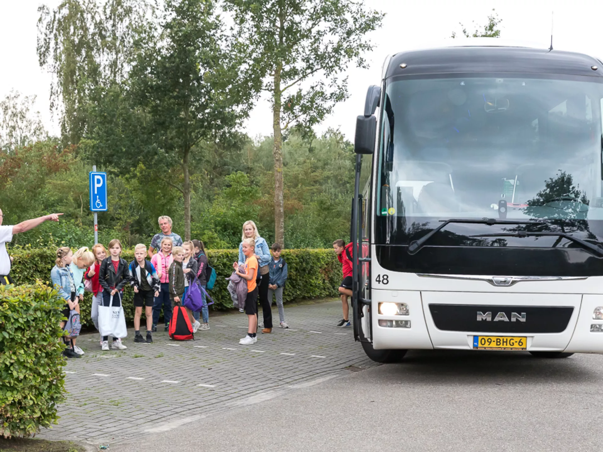 Groep kinderen naast een bus, klaar om op reis te gaan.