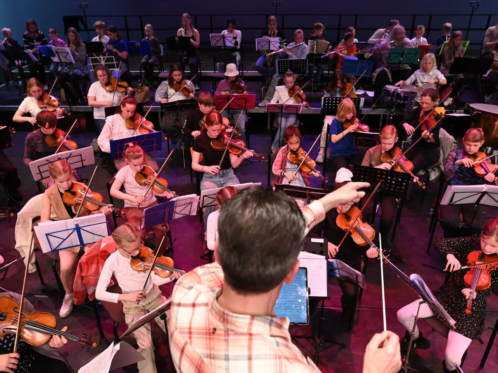 Kinderorkestleden spelen viool onder leiding van de dirigent.