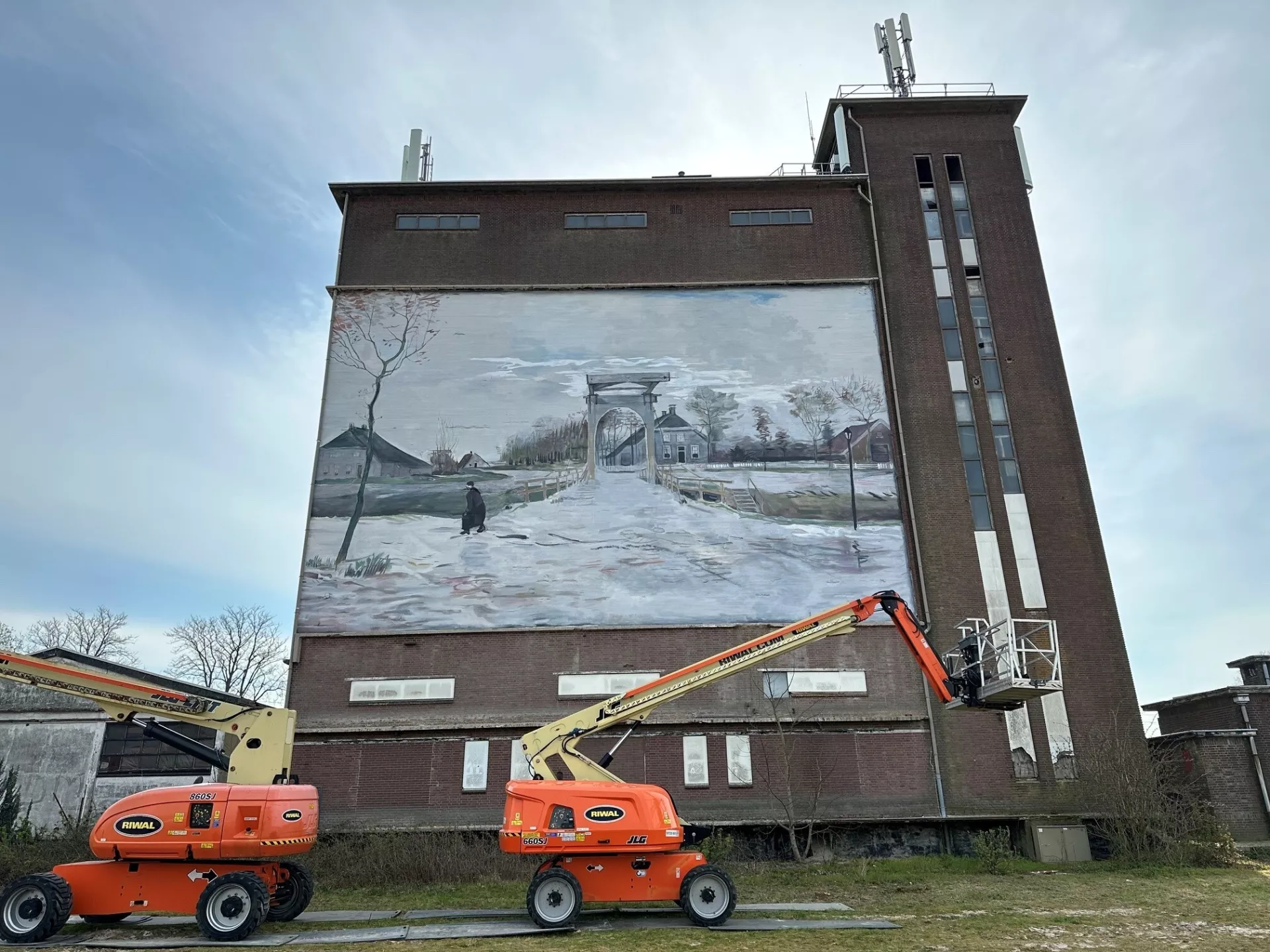 Muurschildering van een winterlandschap op een gebouw met twee hoogwerkers ervoor.