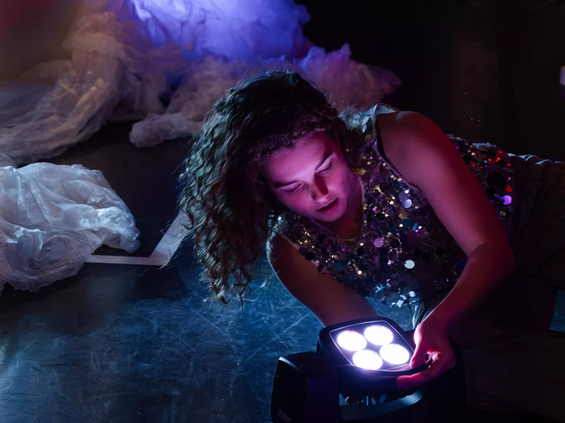 Vrouw onderzoekt een kleurrijke lamp in een donkere ruimte.