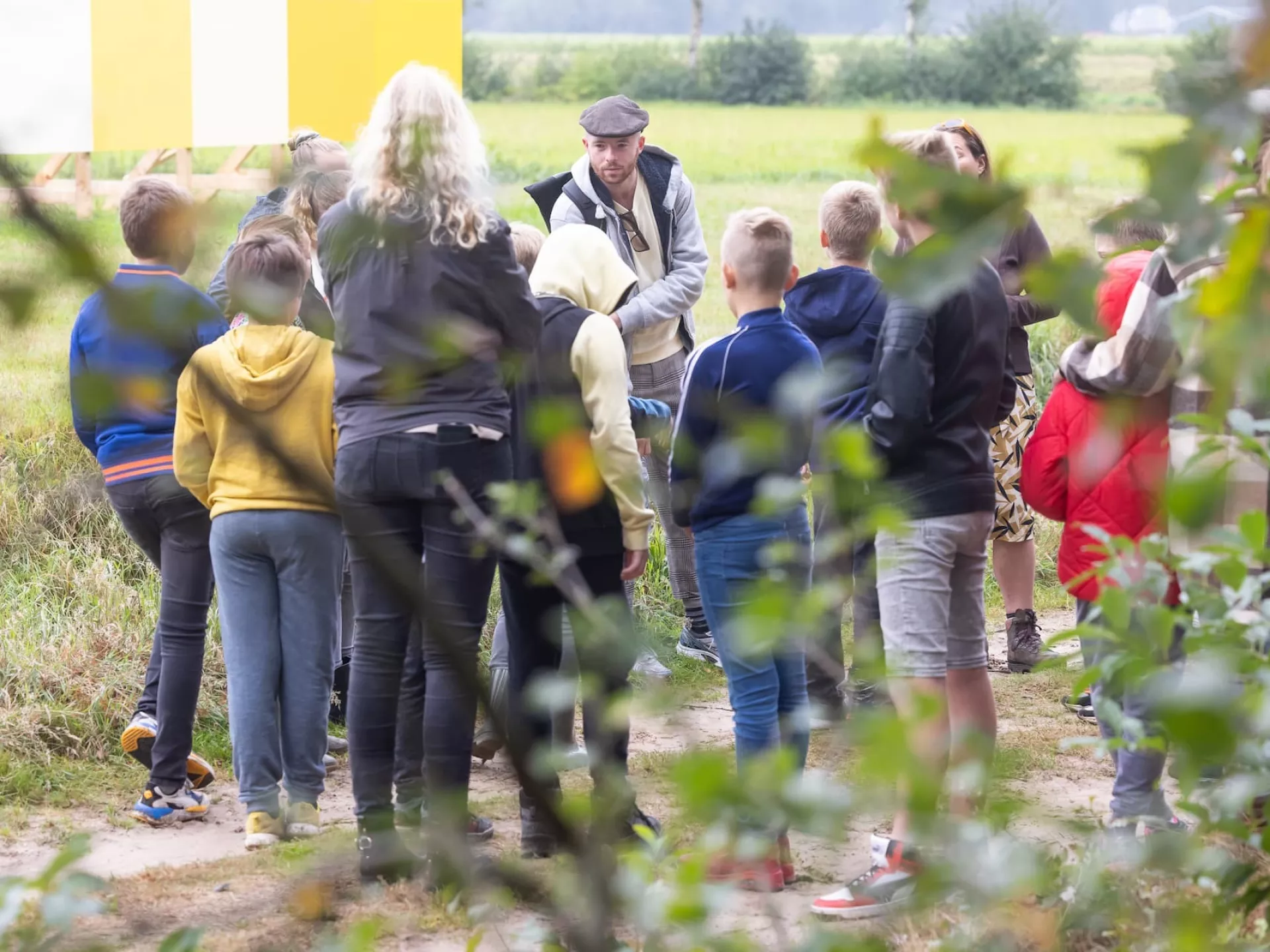 Groep kinderen luistert naar een gids in een veld.