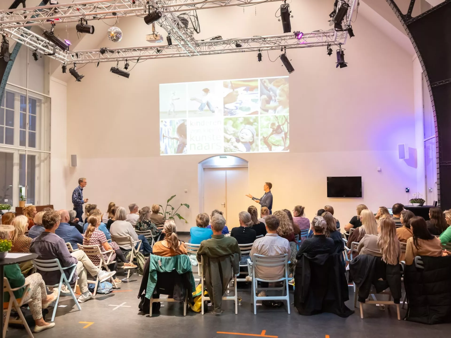 Mensen luisteren naar een presentatie in een verlichte zaal.
