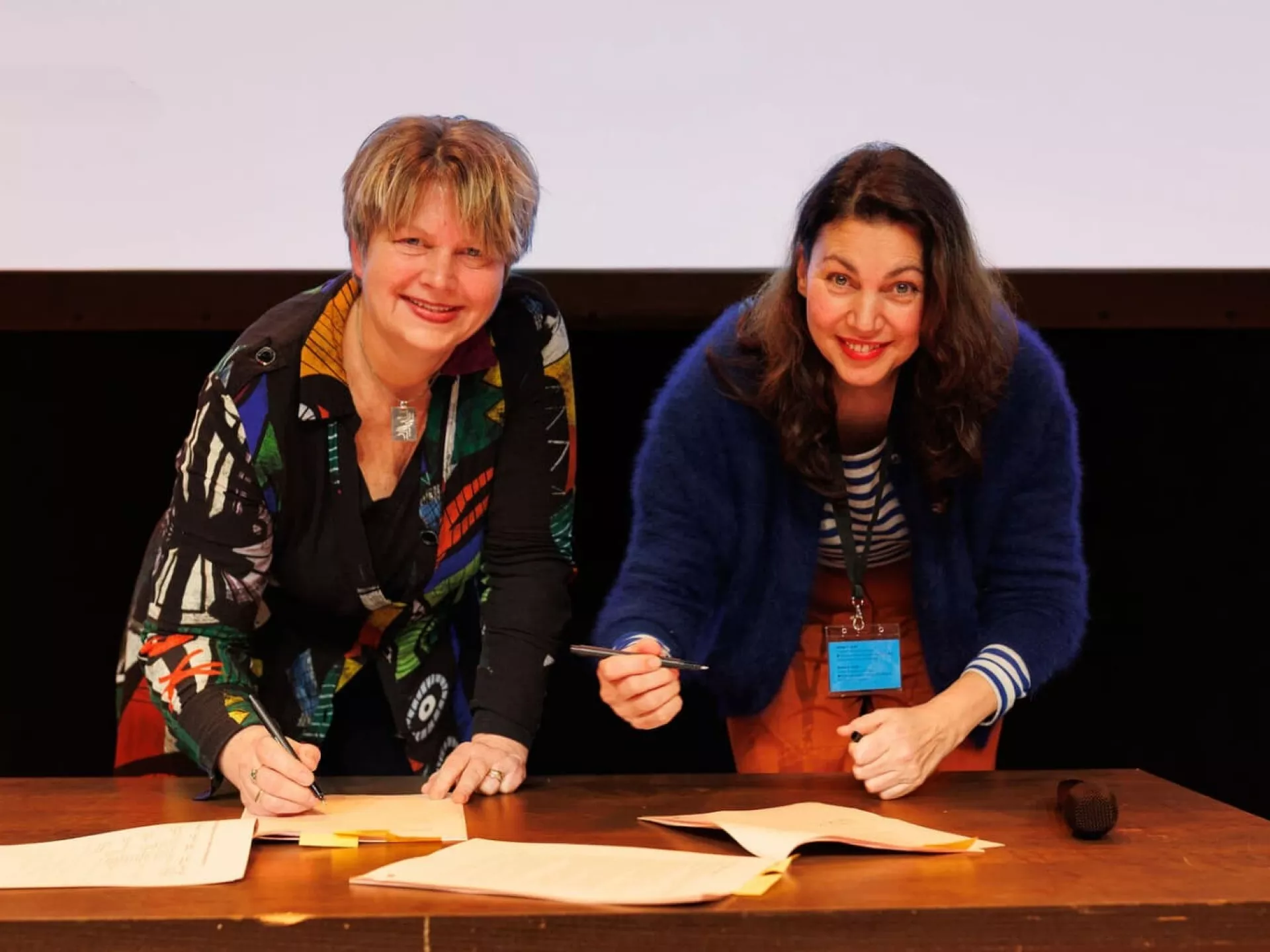 Twee vrouwen die documenten ondertekenen aan een tafel.