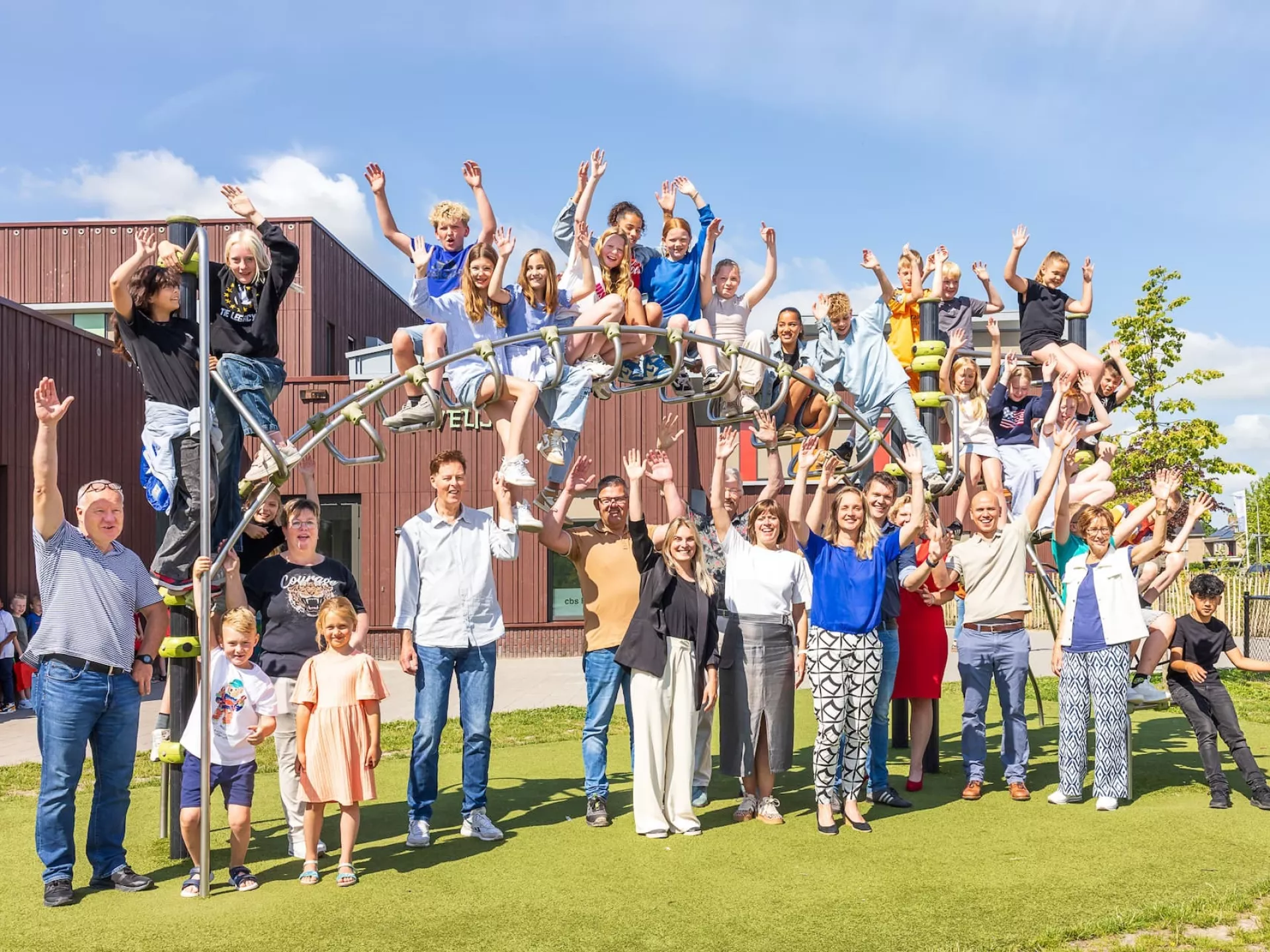 Juichende kinderen en leerkrachten rond een klimtoestel op het schoolplein.