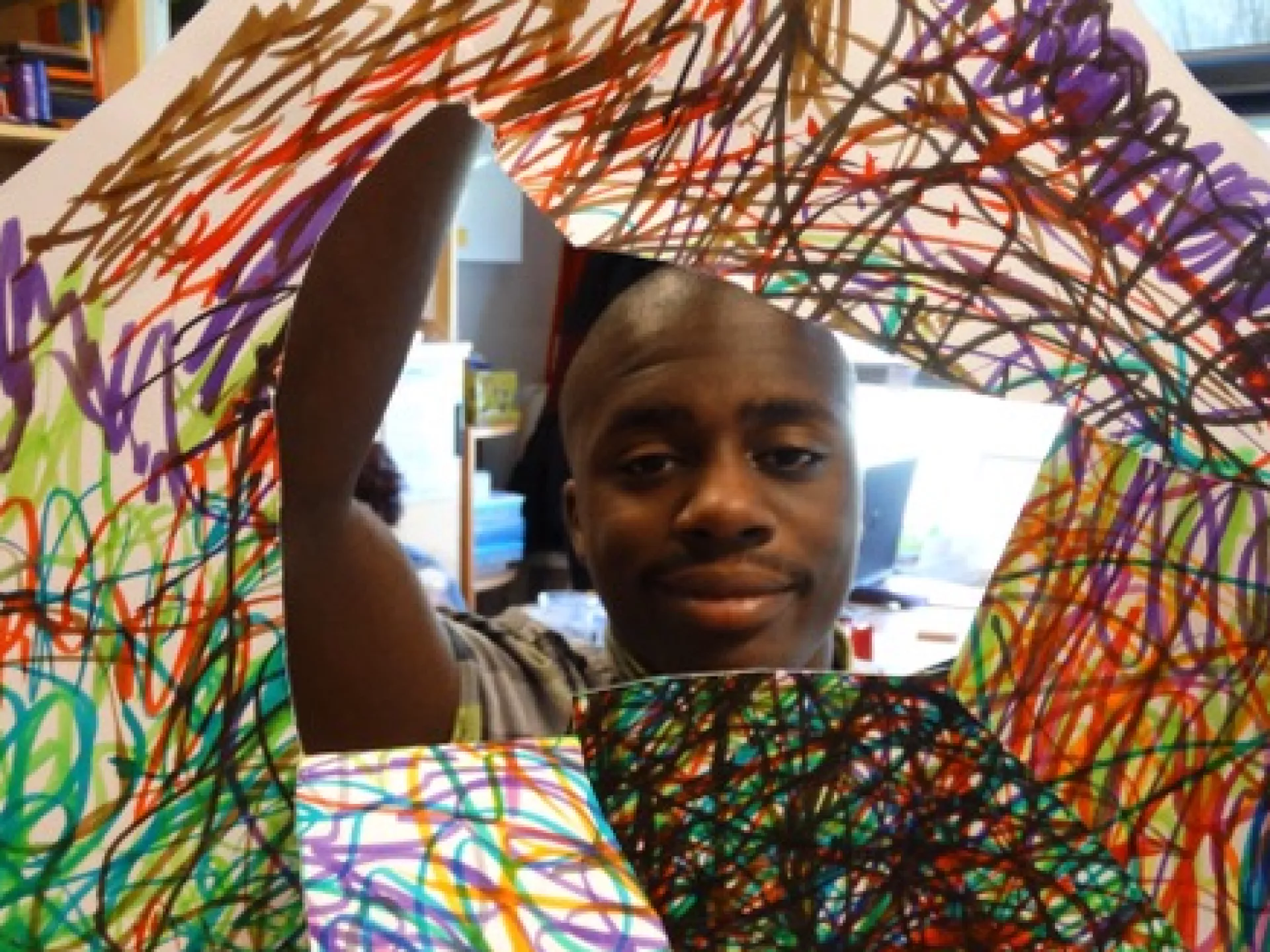 Een jongen toont een kleurrijk kunstwerk met krabbels.