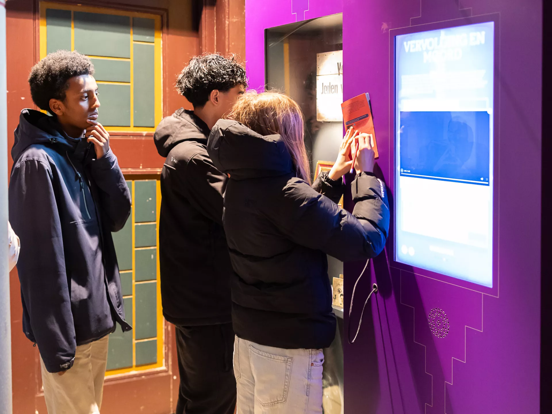 Drie jonge mensen gebruiken een interactieve terminal op een paarse achtergrond.