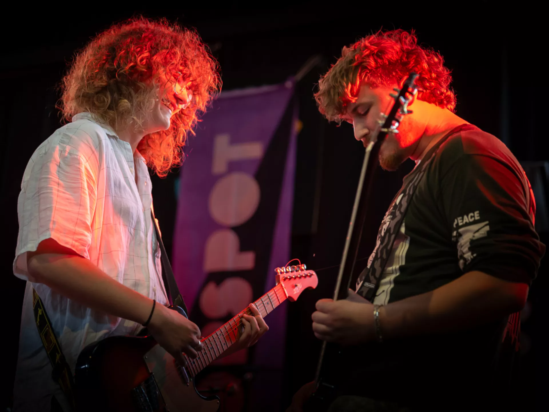 Twee muzikanten spelen gitaar op een podium.