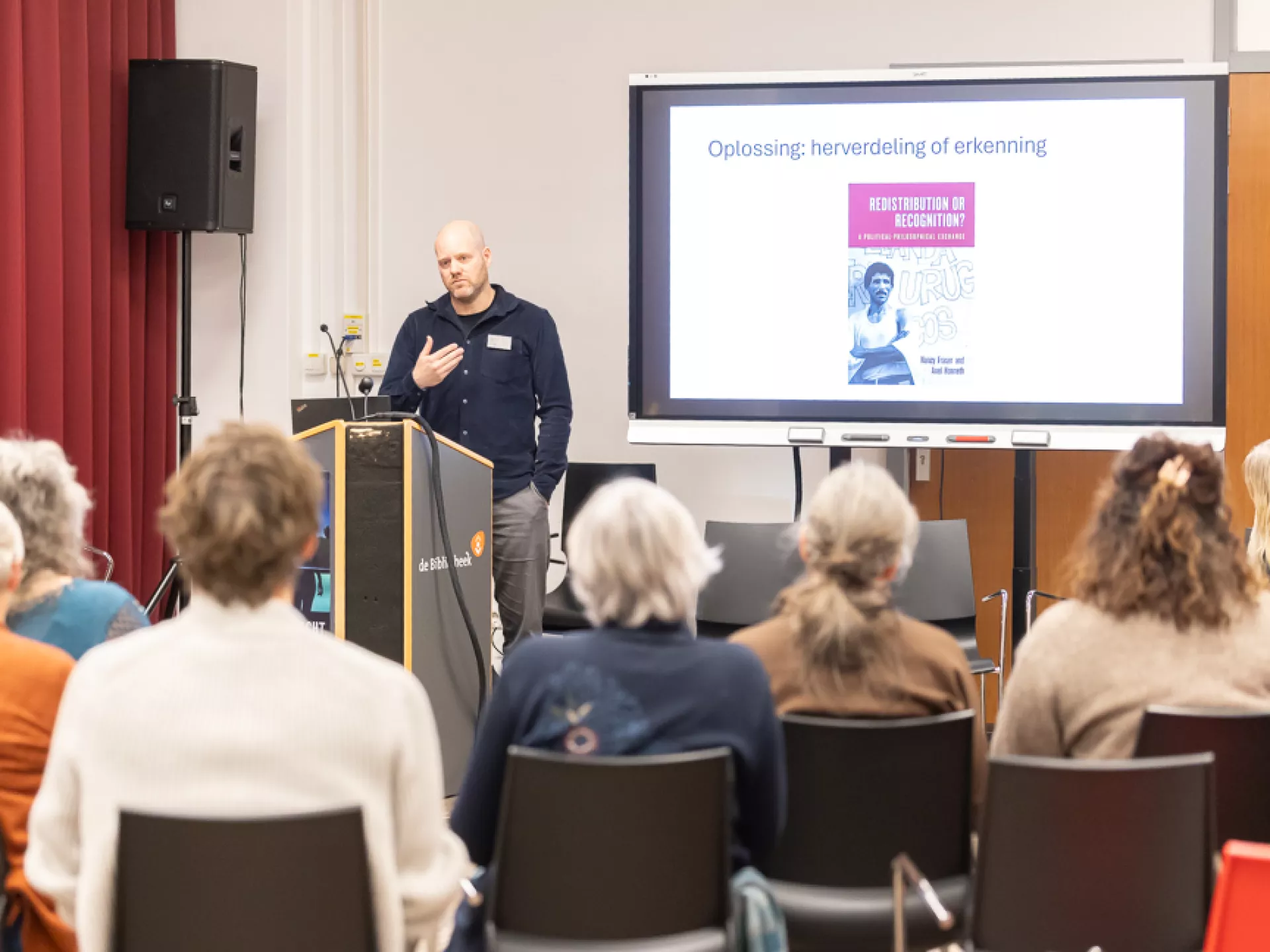 Een spreker presenteert voor een publiek in een vergaderruimte.