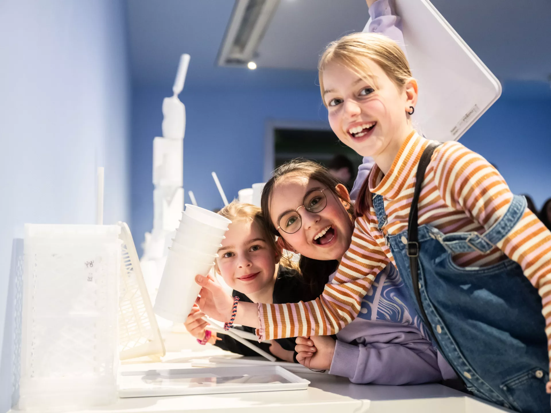 Drie lachende kinderen genieten van een interactieve tentoonstelling.