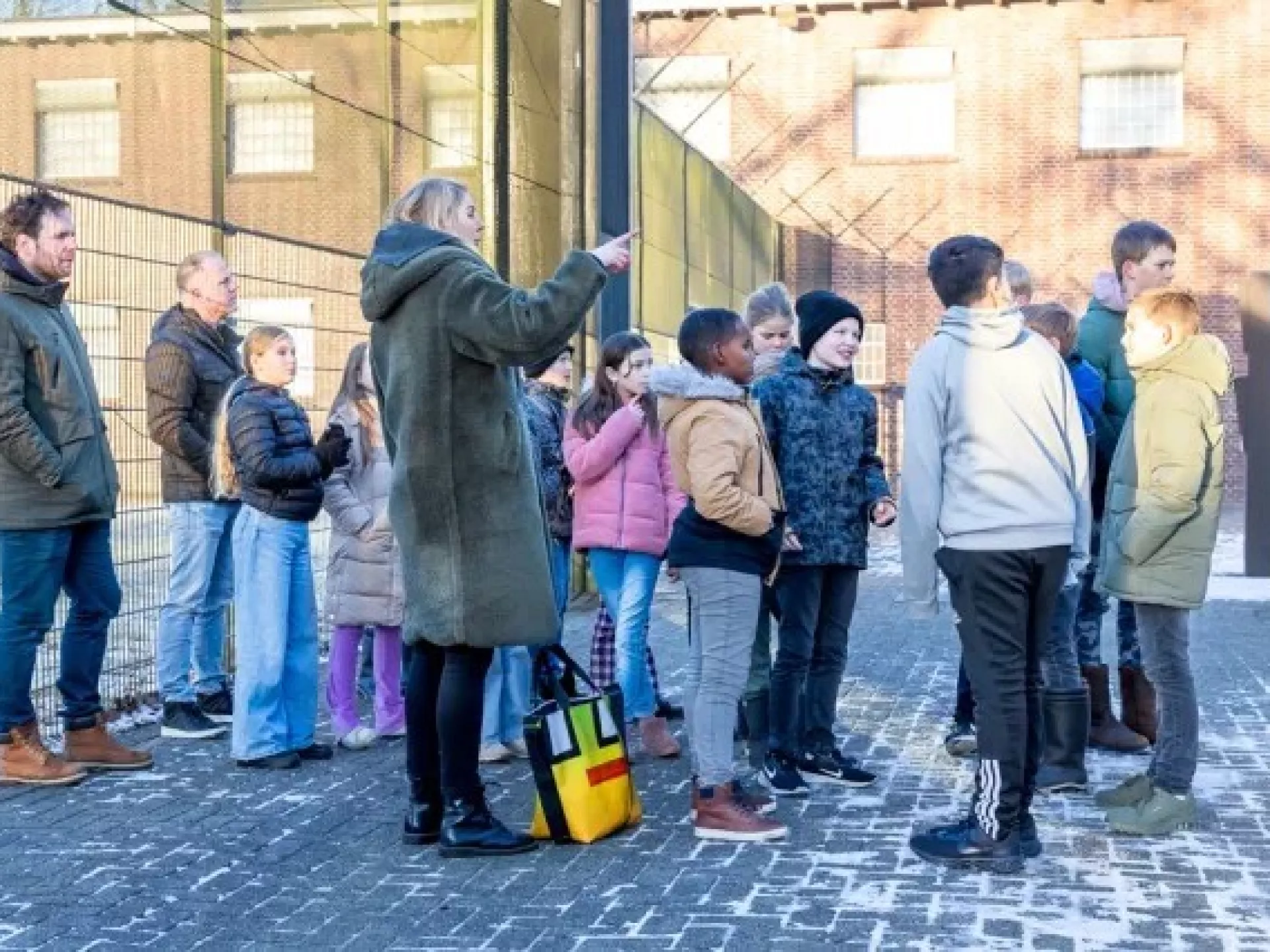 Een groep kinderen en een paar volwassenen staan buiten bij een hek.