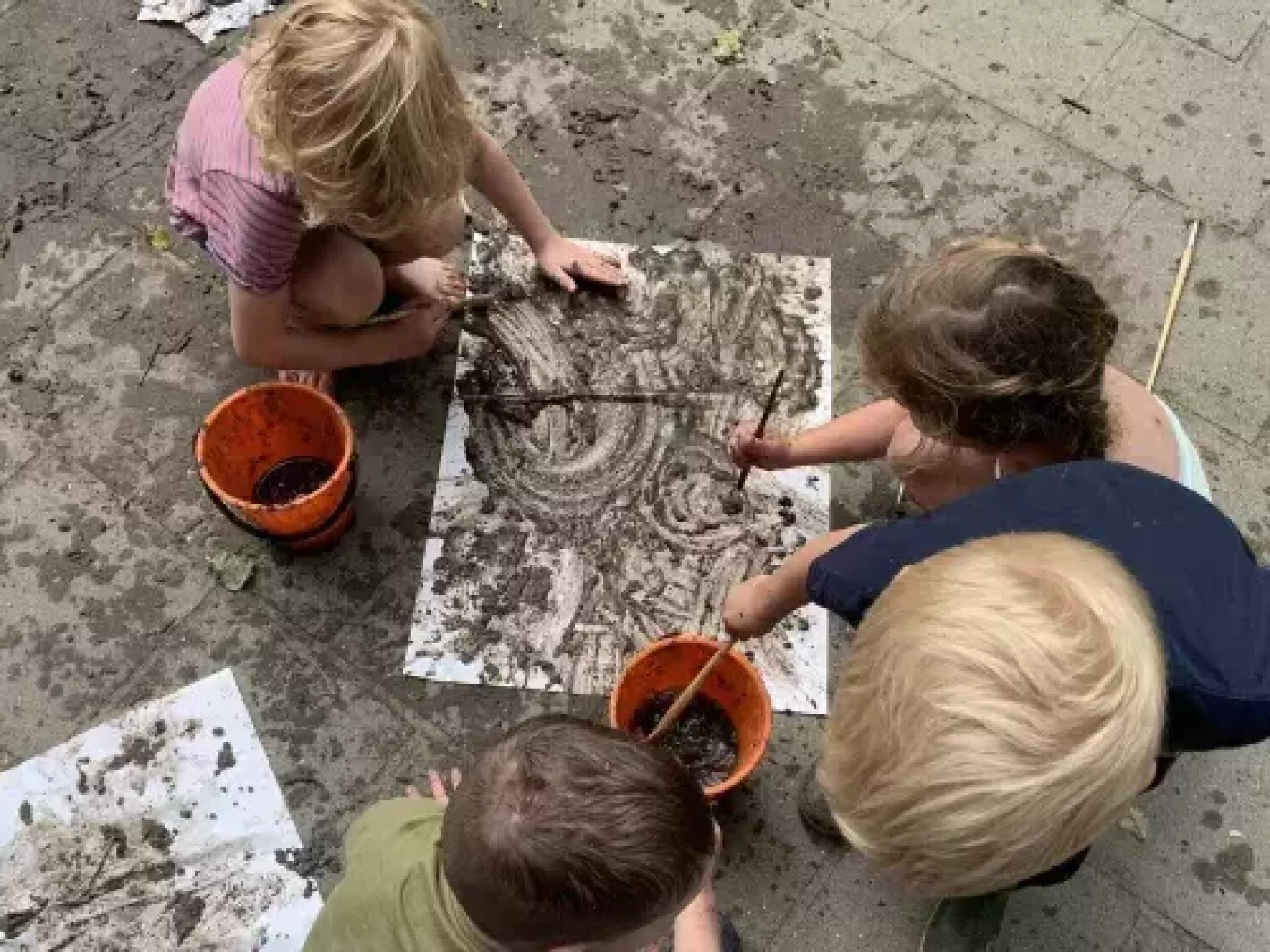 Kinderen maken kunst met modder op papier.
