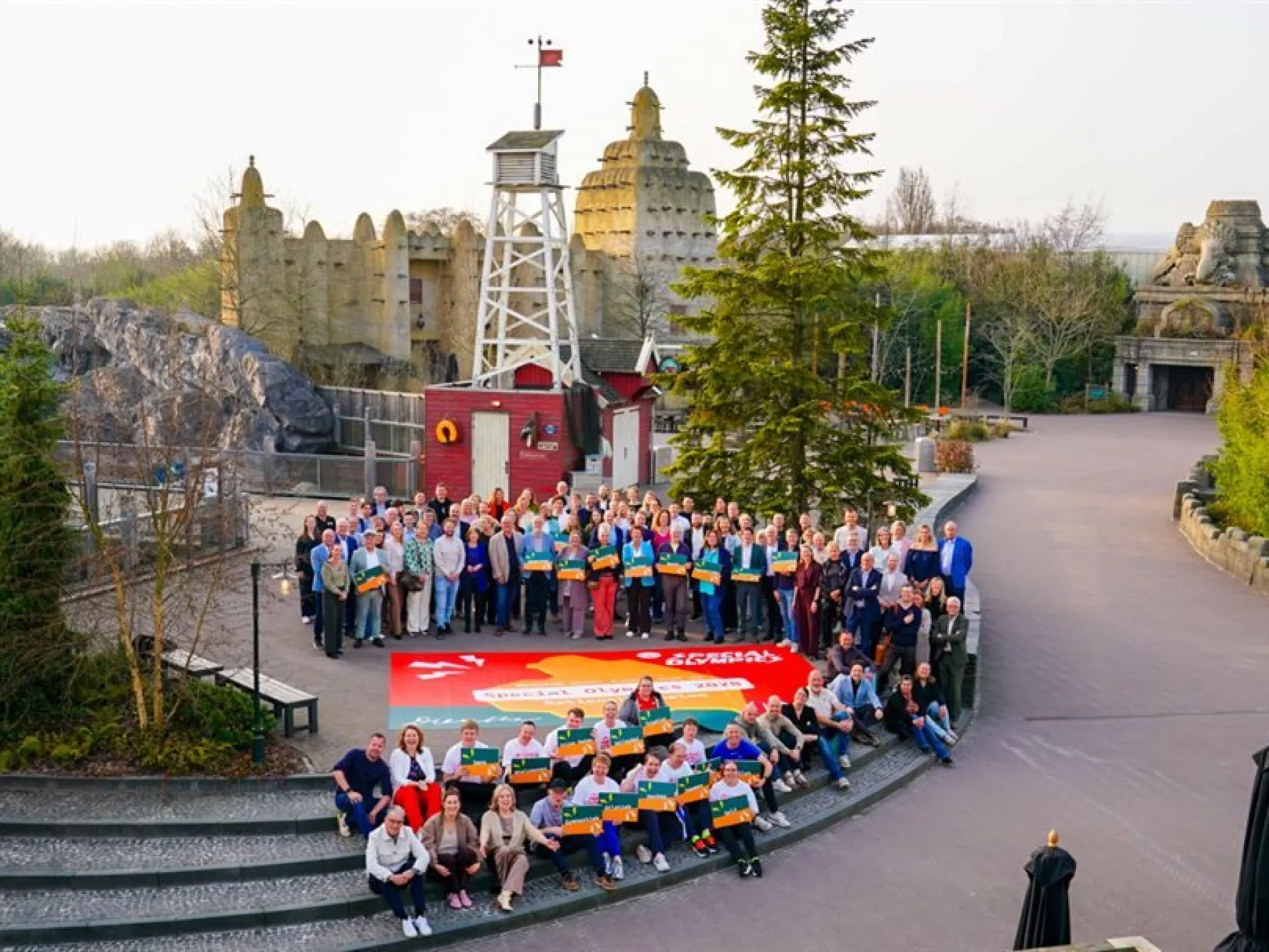 Een grote groep mensen poseert voor een kleurrijke achtergrond in een themapark.