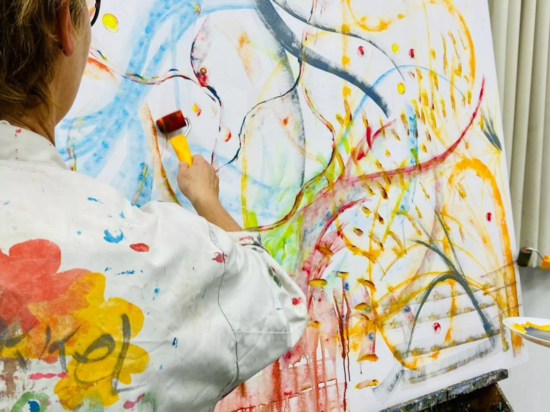 Een persoon schildert met kleurrijke verf op een groot doek.