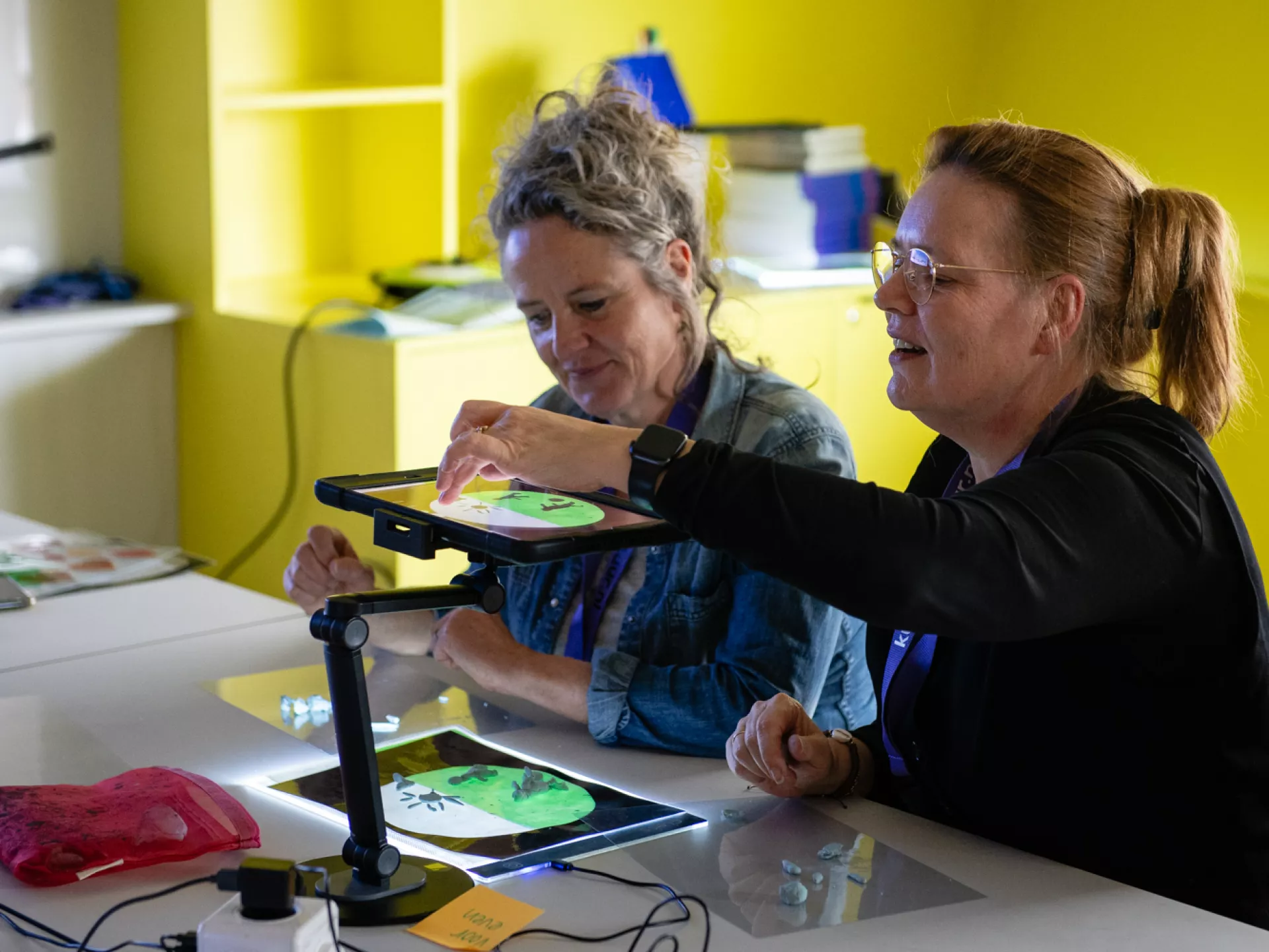 Twee vrouwen werken samen aan een project met behulp van een tablet in een creatieve ruimte.