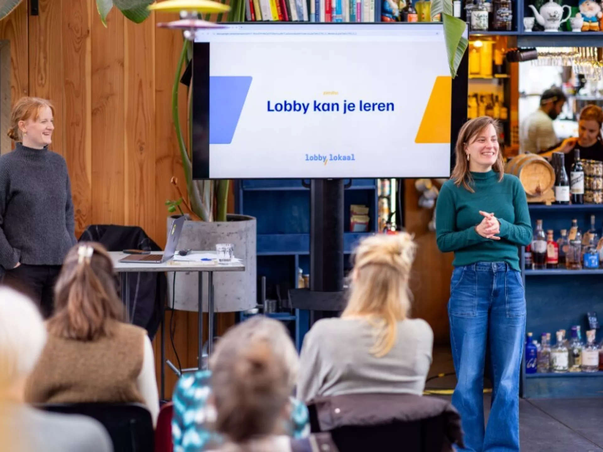 Een spreker presenteert voor een klein publiek in een informele ruimte.