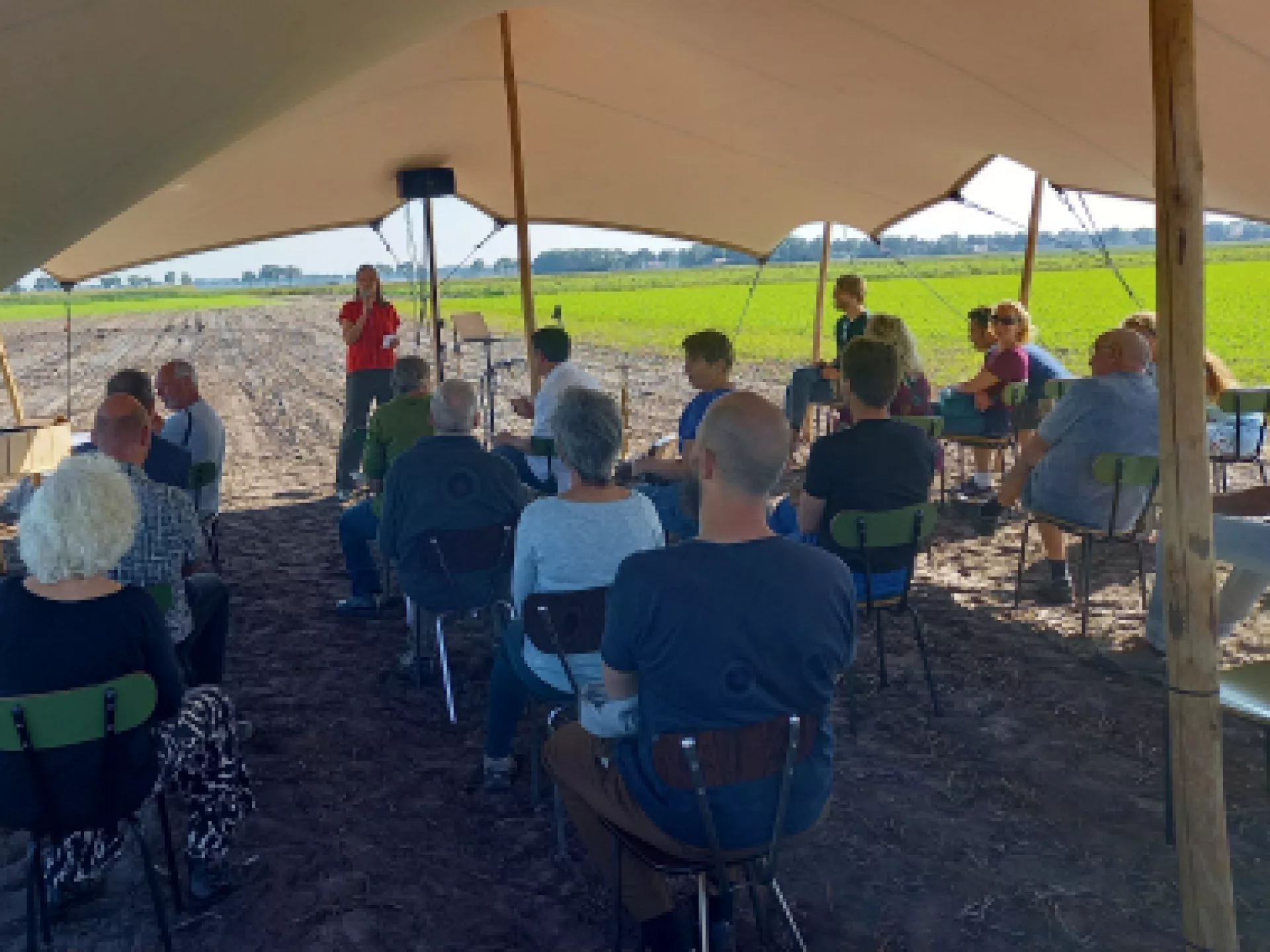 Groep mensen onder een tent op een veldbijeenkomst.
