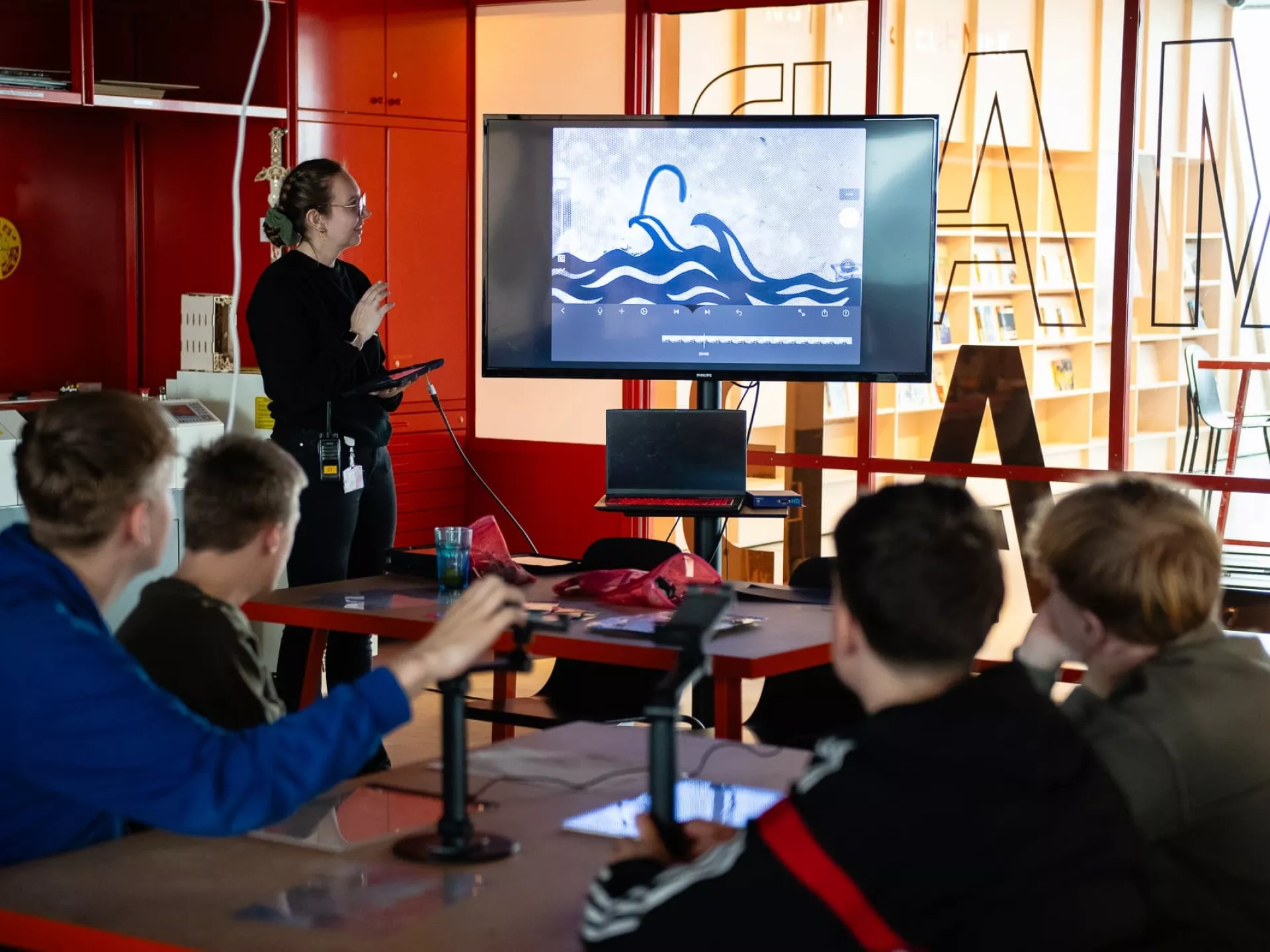 Een groep jongeren kijkt naar een presentatie op een scherm in een klaslokaal.