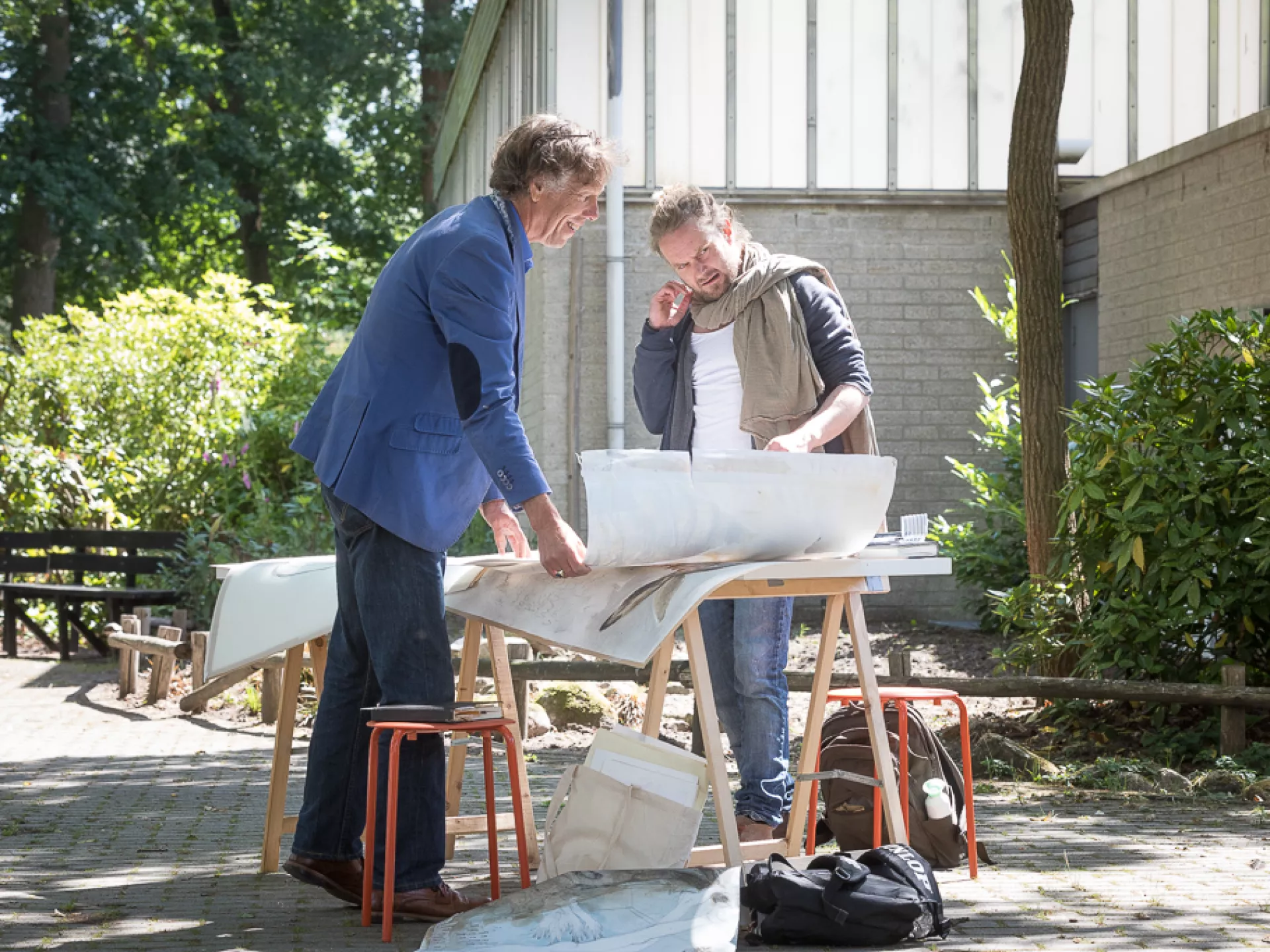 Twee mannen bespreken een bouwmodel buiten op een zonnige dag.