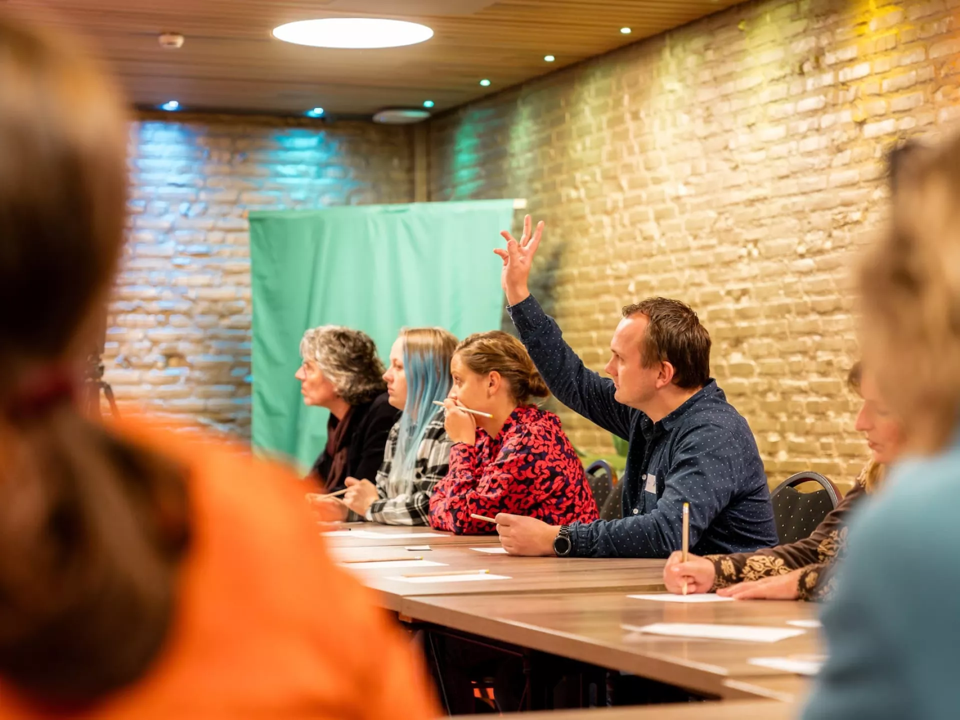 Een man steekt zijn hand op tijdens een cursus aan een lang tafel.