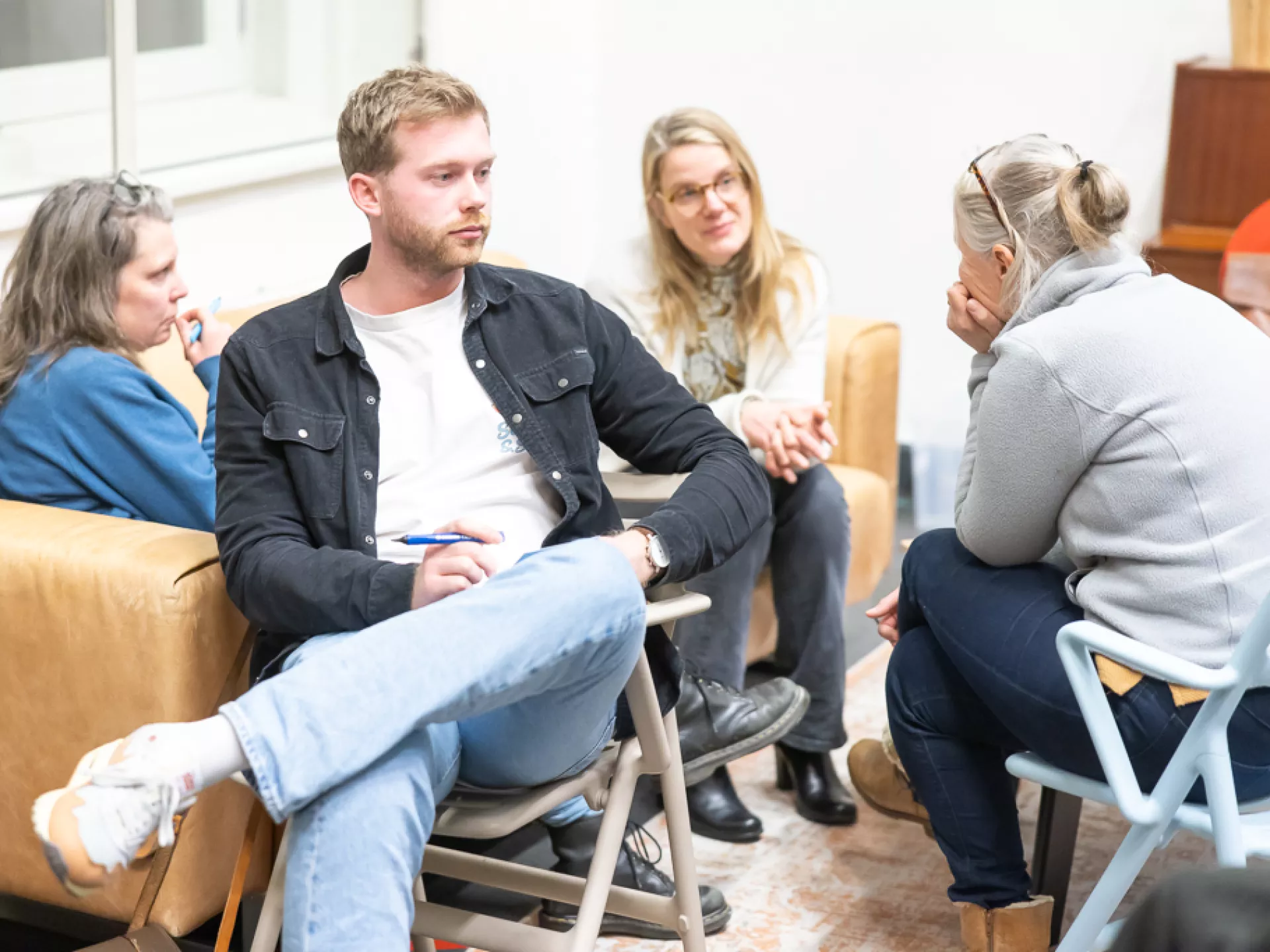 Een groep mensen in een gesprek zittend op stoelen in een kamer.