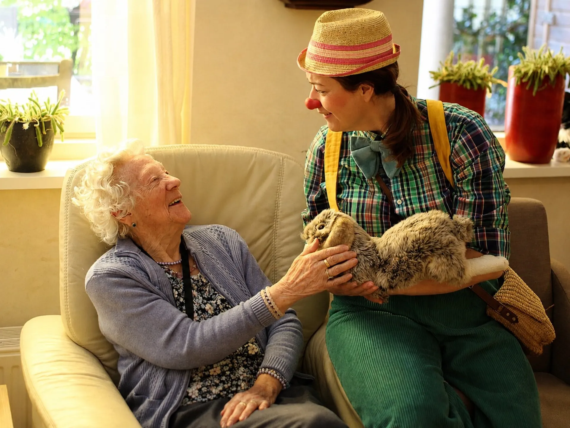 Een oudere vrouw glimlacht terwijl ze met Zorgclown Cato in een speelse outfit praat.