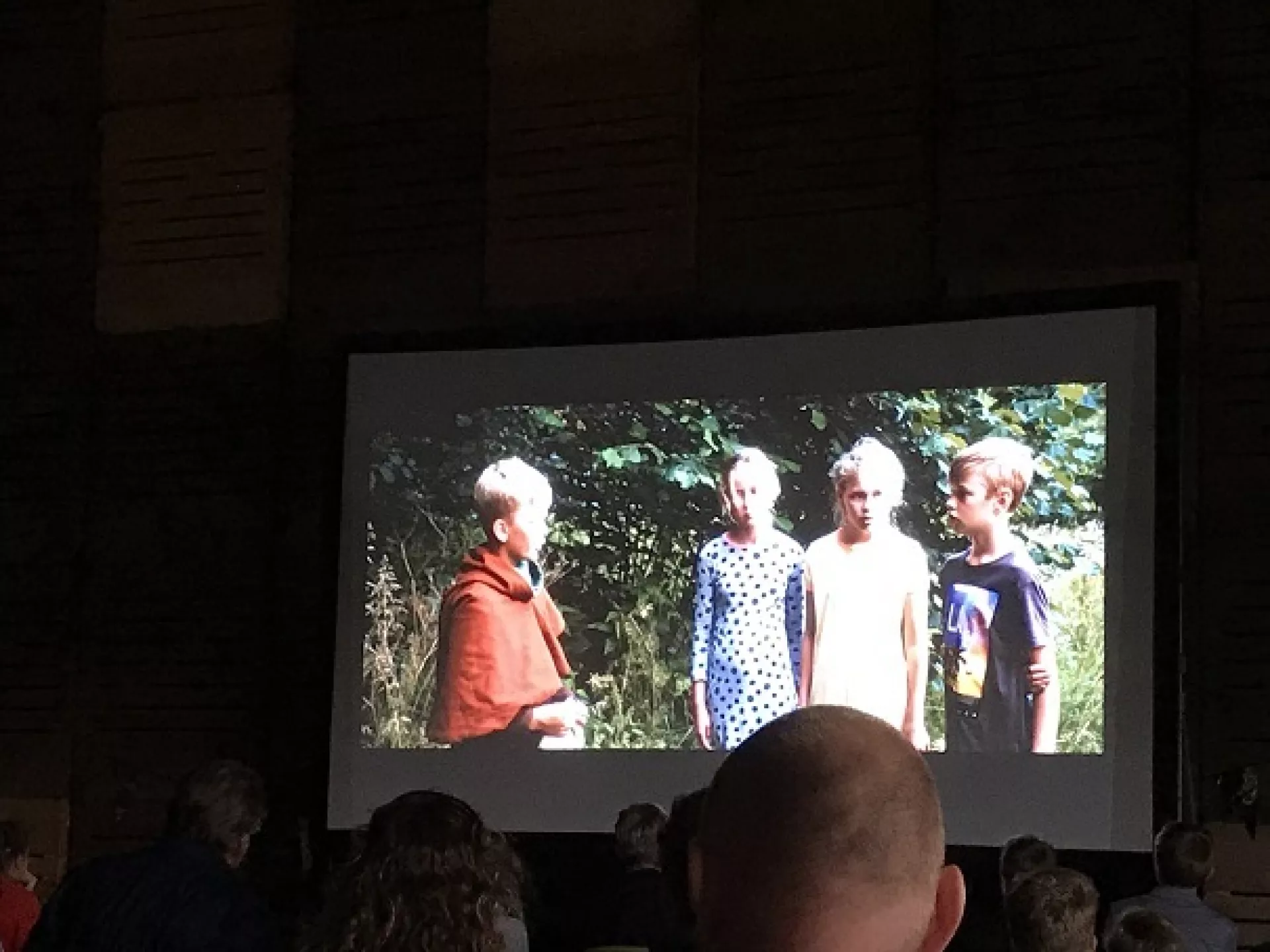 Een groep mensen kijkt naar een filmprojectie van kinderen buiten.