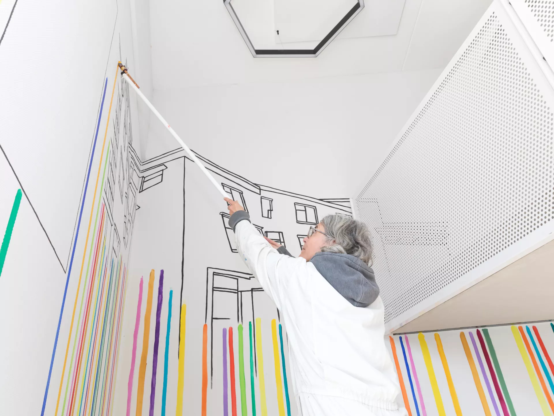 Een kunstenaar schildert een kleurrijke muurschildering in een interieur.