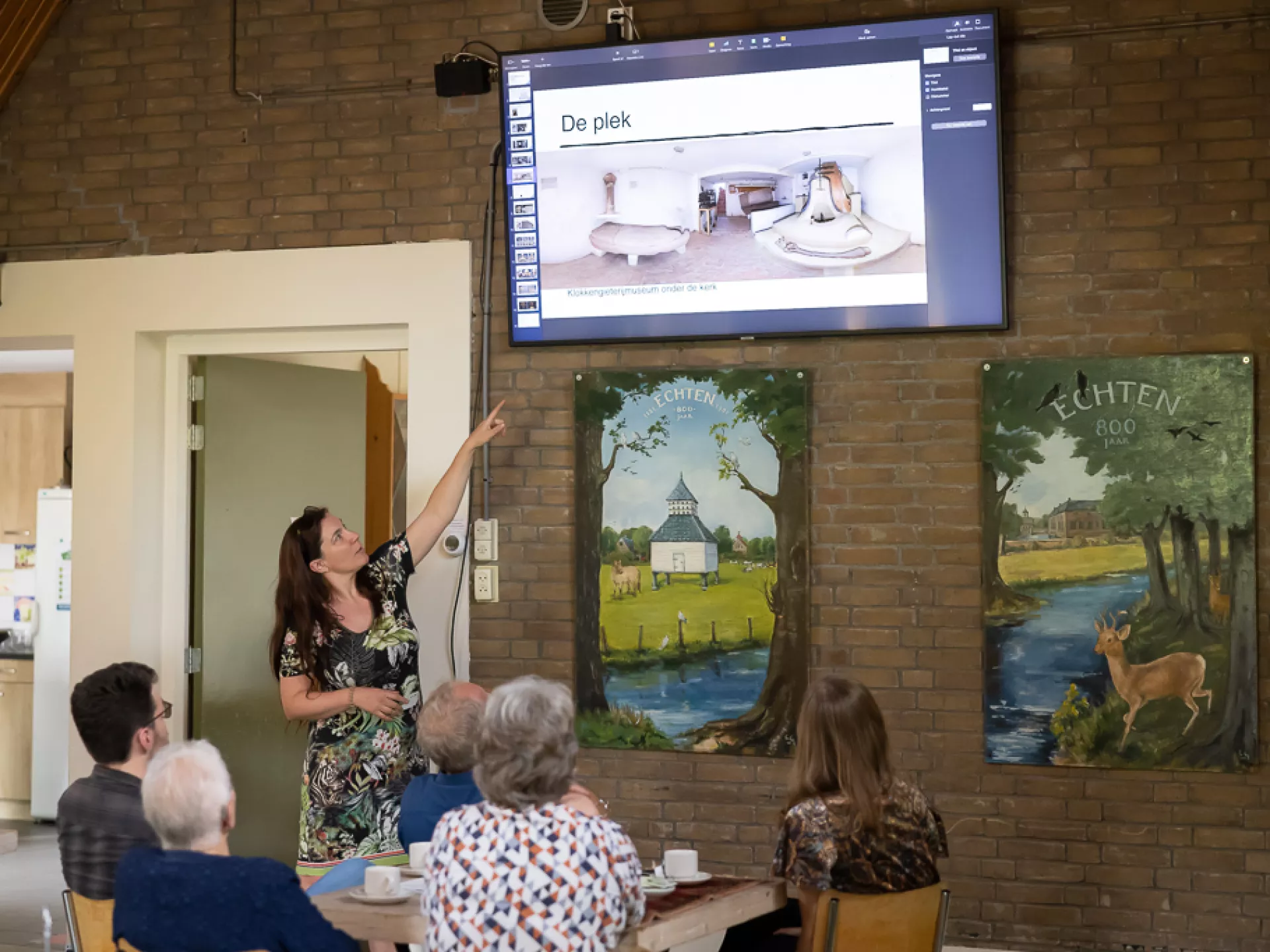 Een vrouw geeft een presentatie aan een groep mensen in een ontmoetingsruimte.