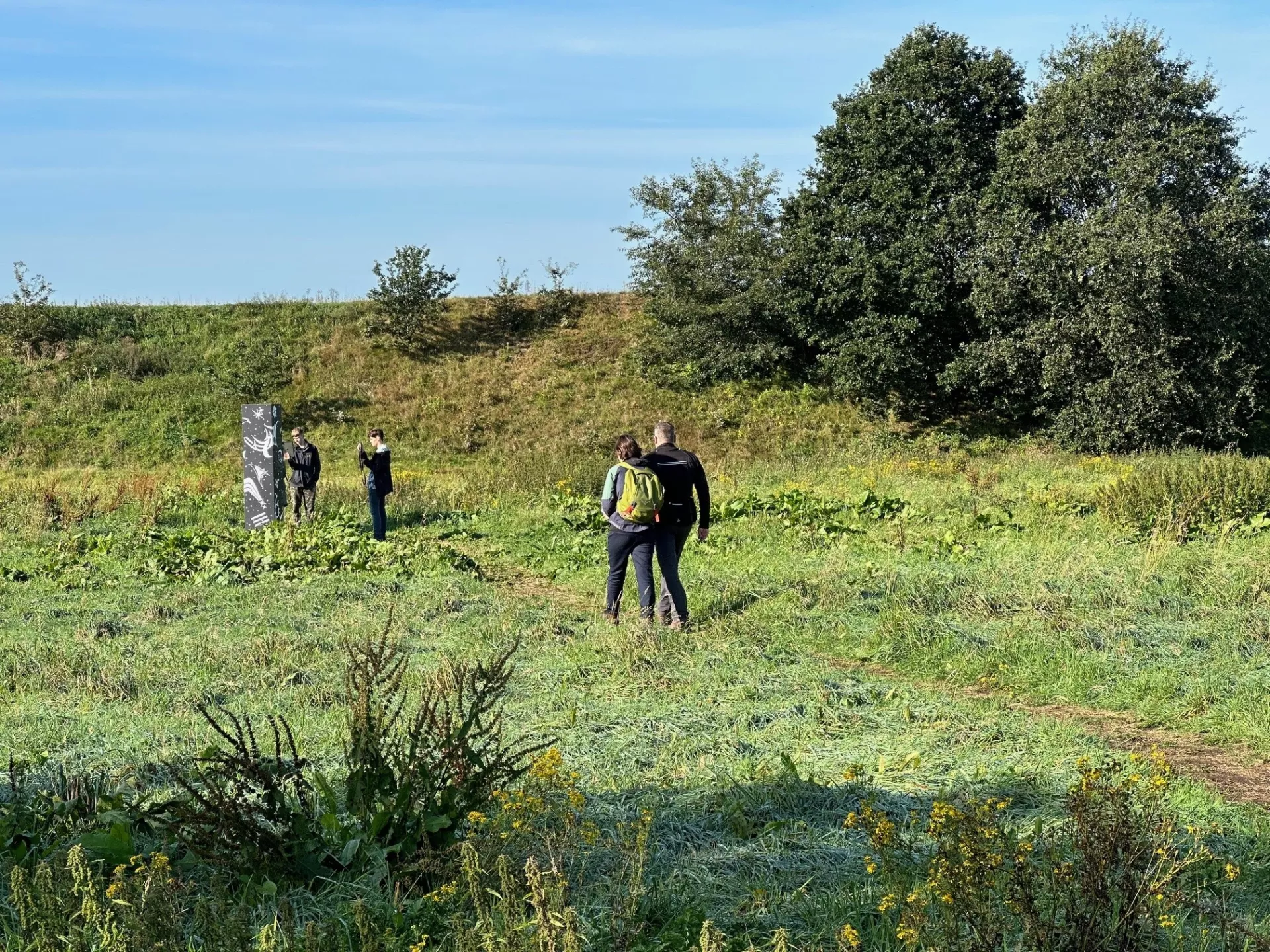 Mensen wandelen in een groen landschap met bomen en een monument op de achtergrond.