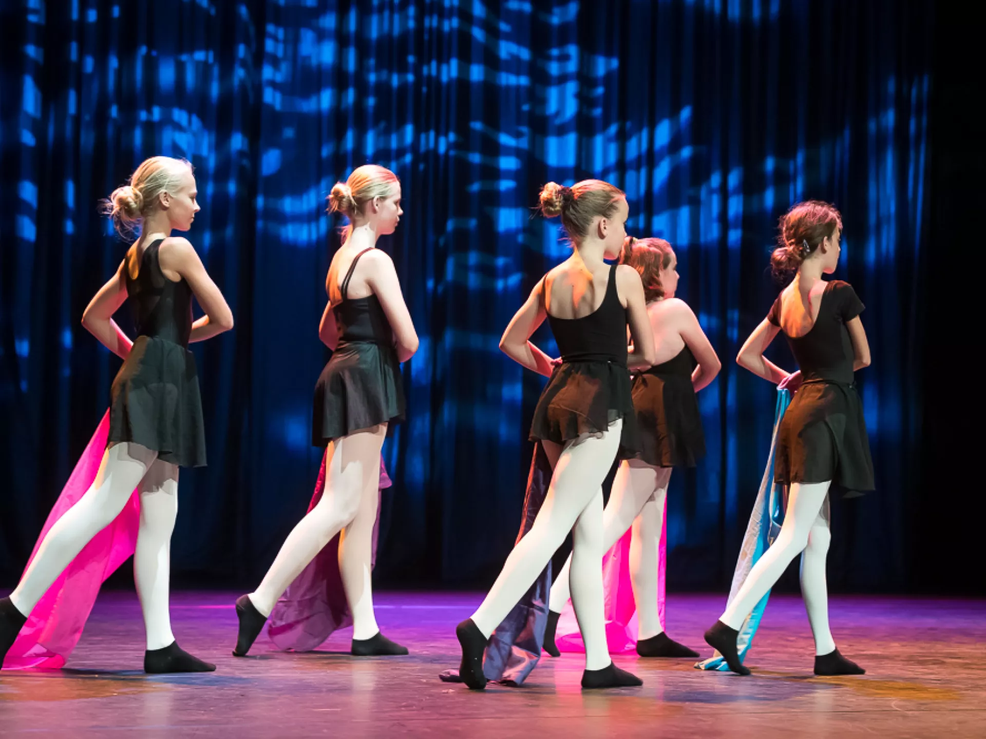 Groep jonge dansers in zwarte kostuums voert een choreografie uit op een podium.