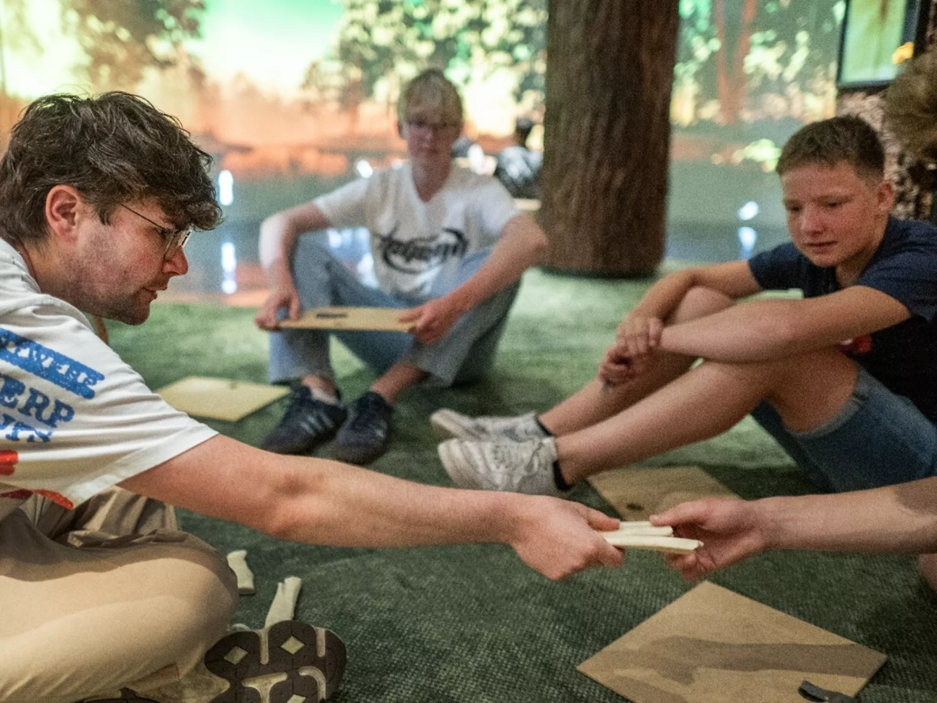 Een groep mensen zit op de grond en deelt houten blokken uit.