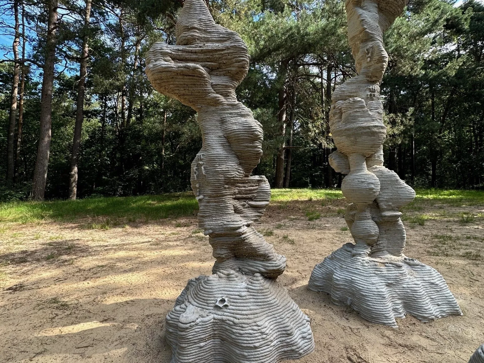 Twee gestapelde sculpturen in een bosrijke omgeving.