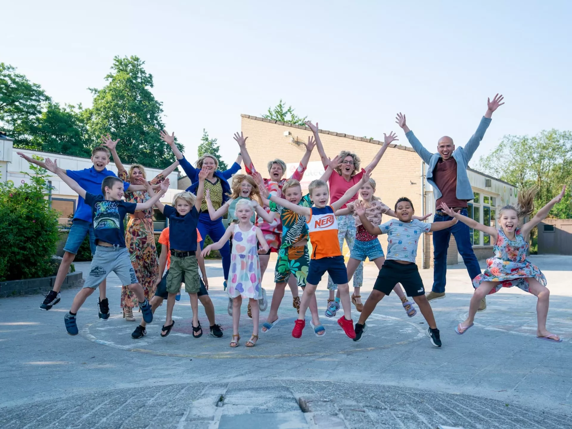 Groep kinderen en een volwassene springen vrolijk in de lucht op een zonnige dag.