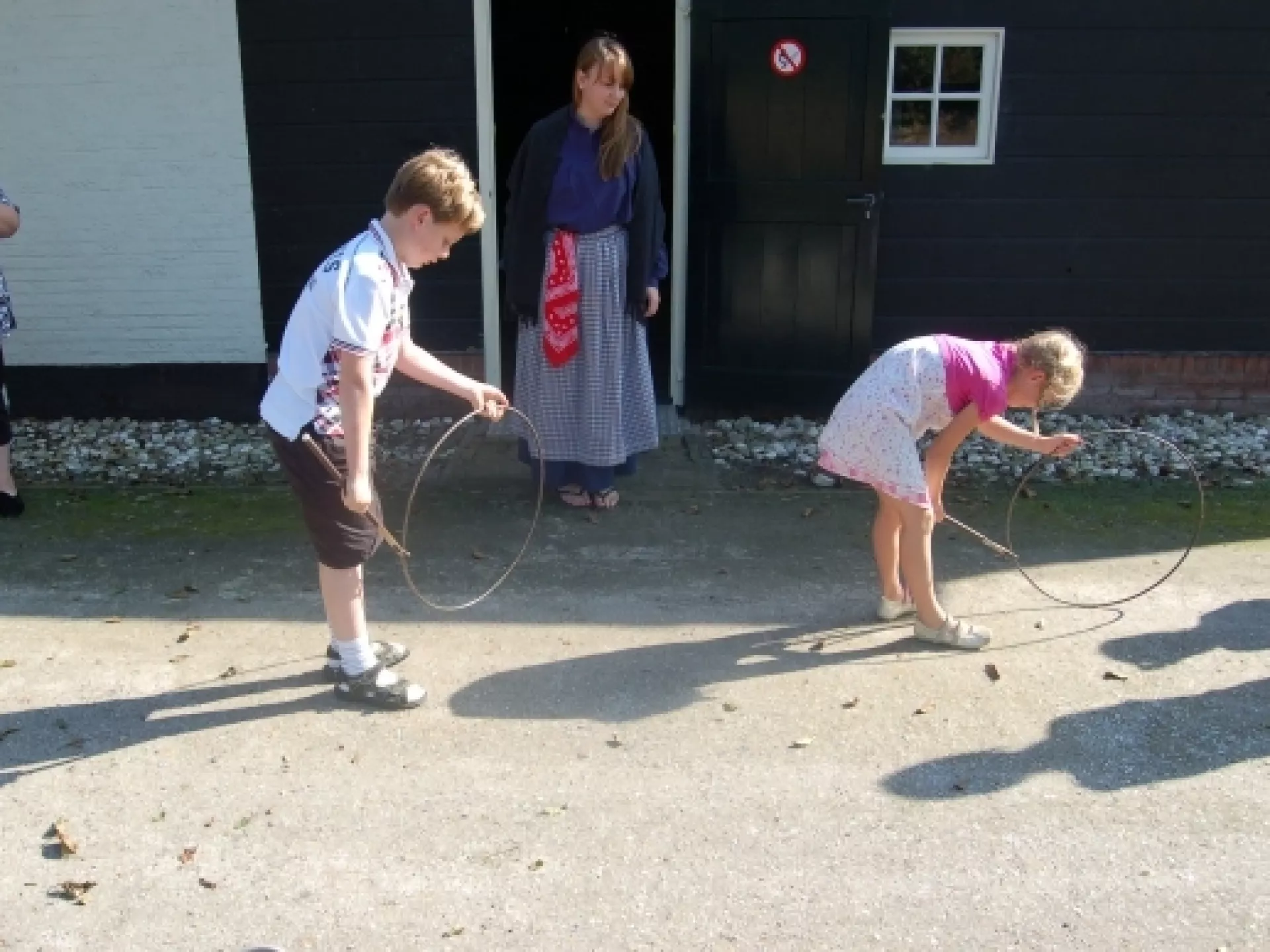 Twee kinderen met ouderwetse hoepel, op achtergrond meisje in klederdracht