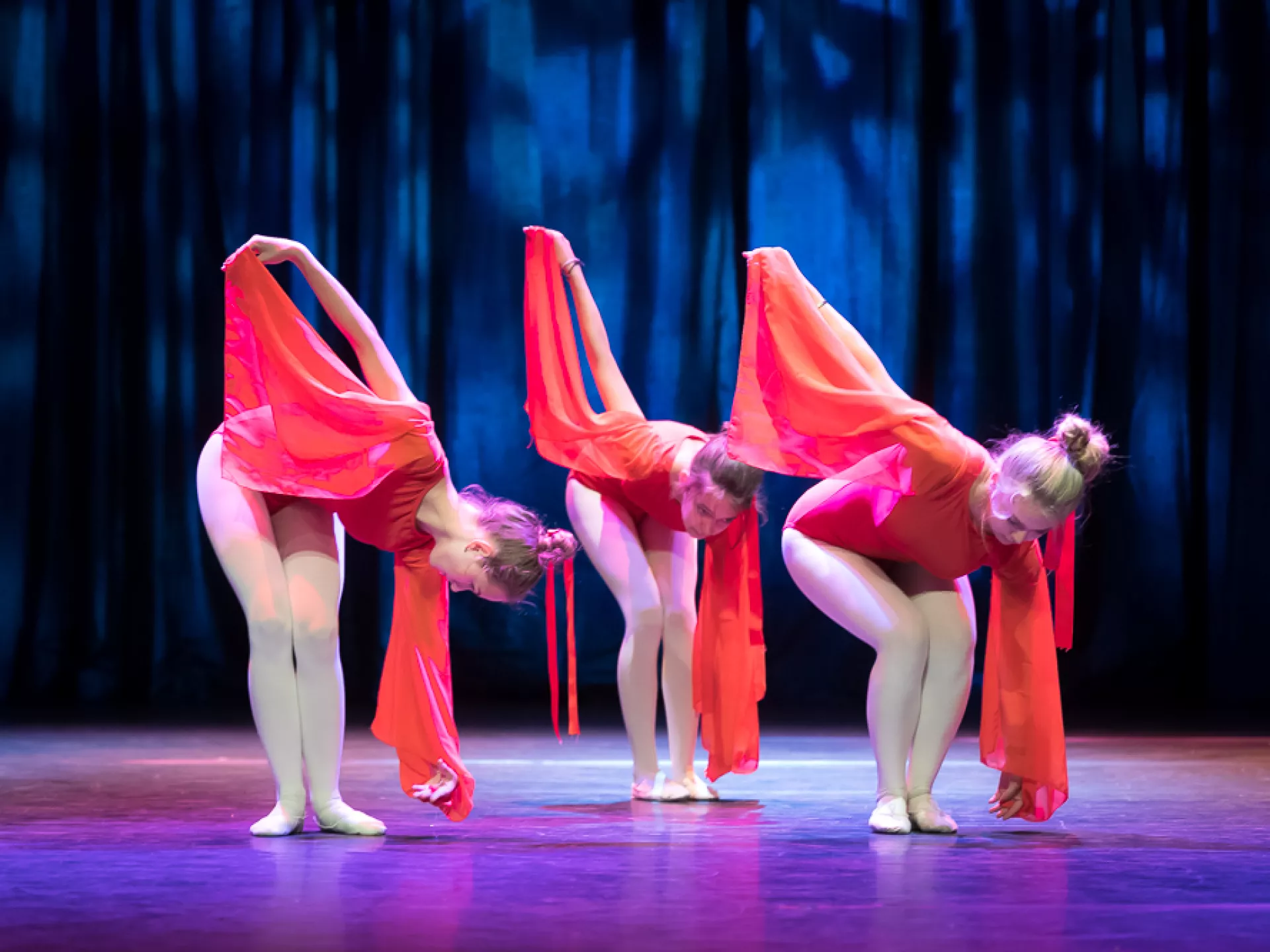 Drie dansers in felrode kostuums buigen voorover op het podium.