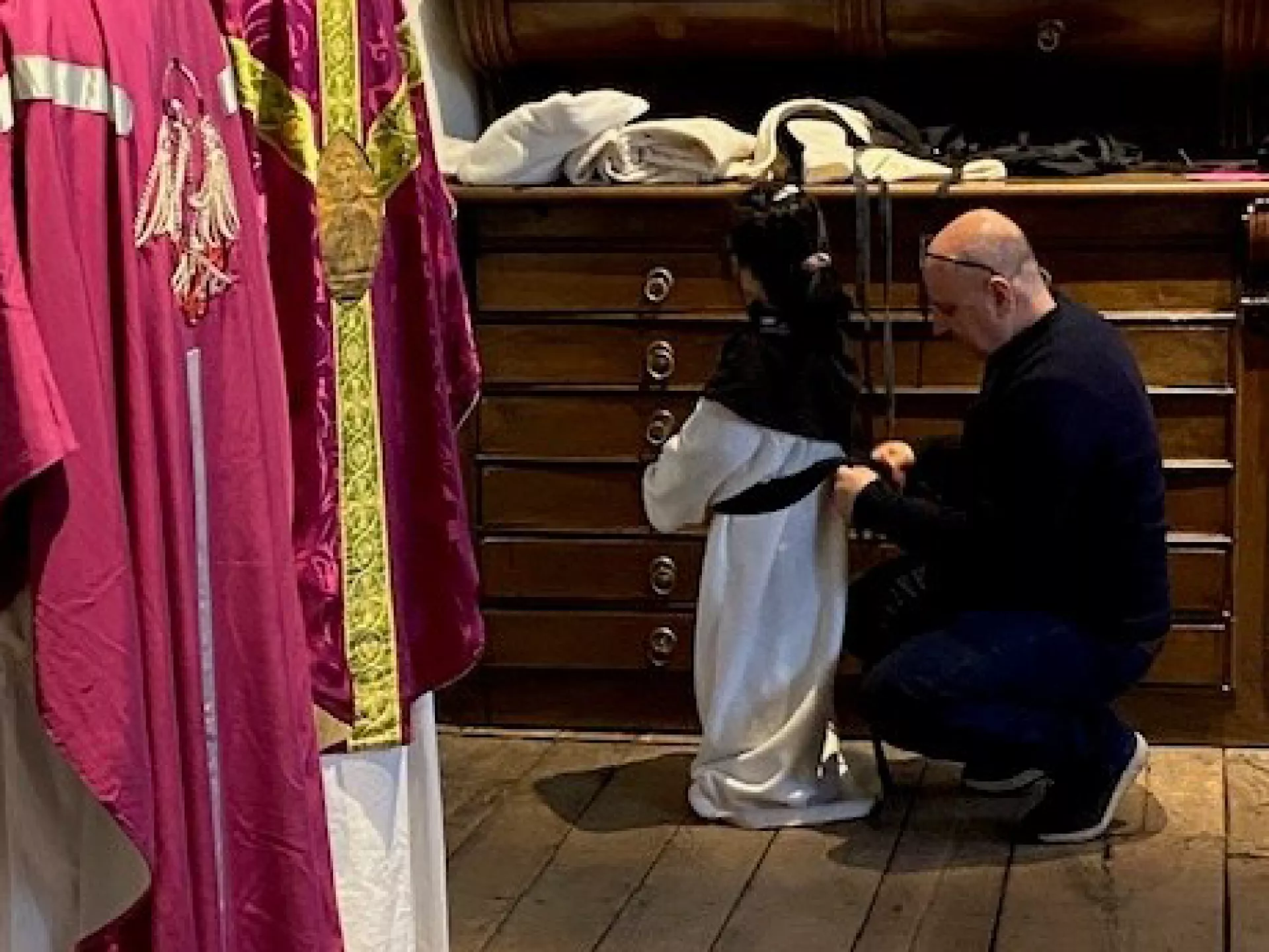 Een man helpt een kind een kerkelijke gewaad aan te trekken.