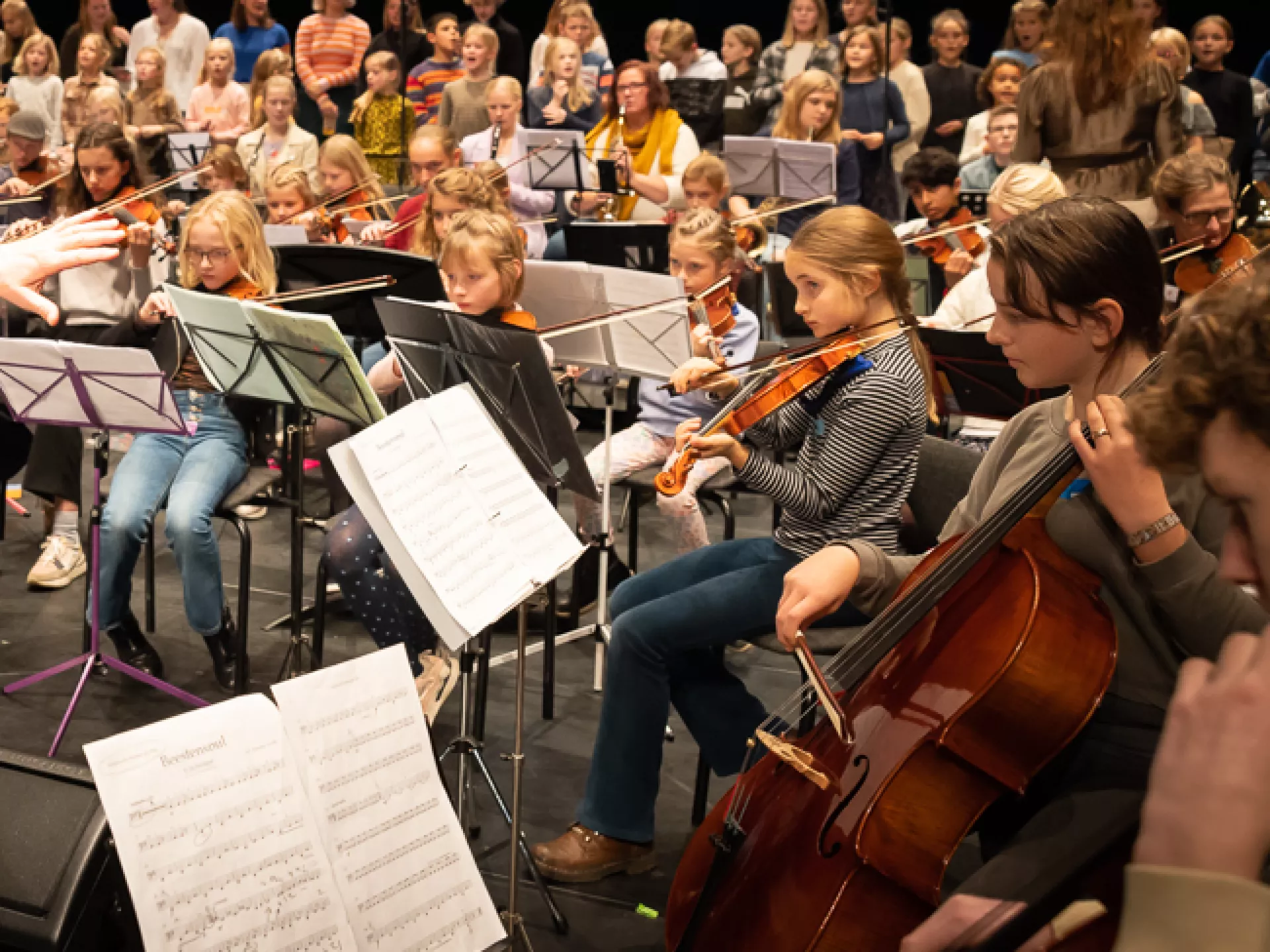Dirigent leidt een orkest van muzikanten en koor op een podium.