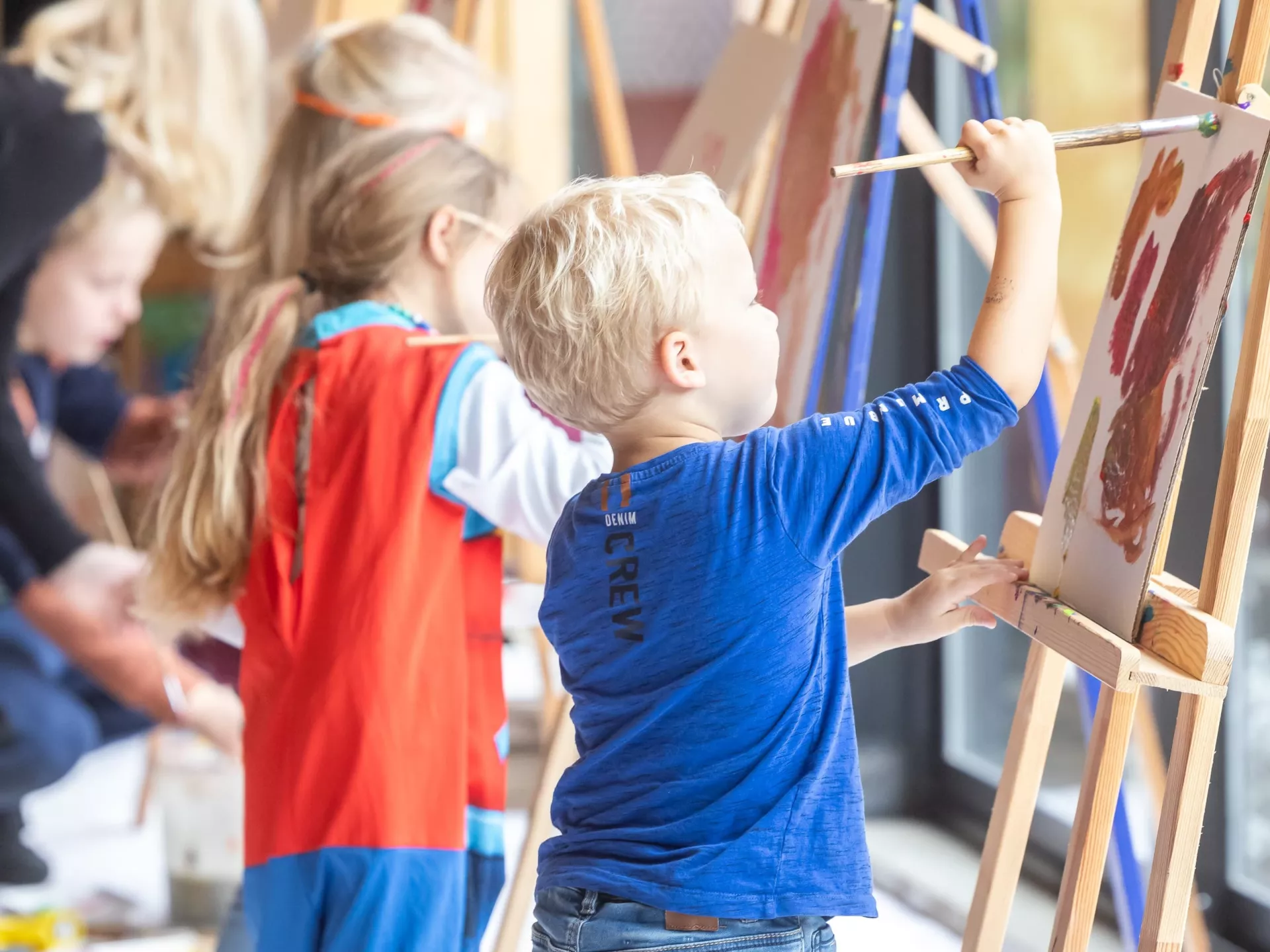 Je ziet twee kinderen die druk schilderen op een schildersezel.