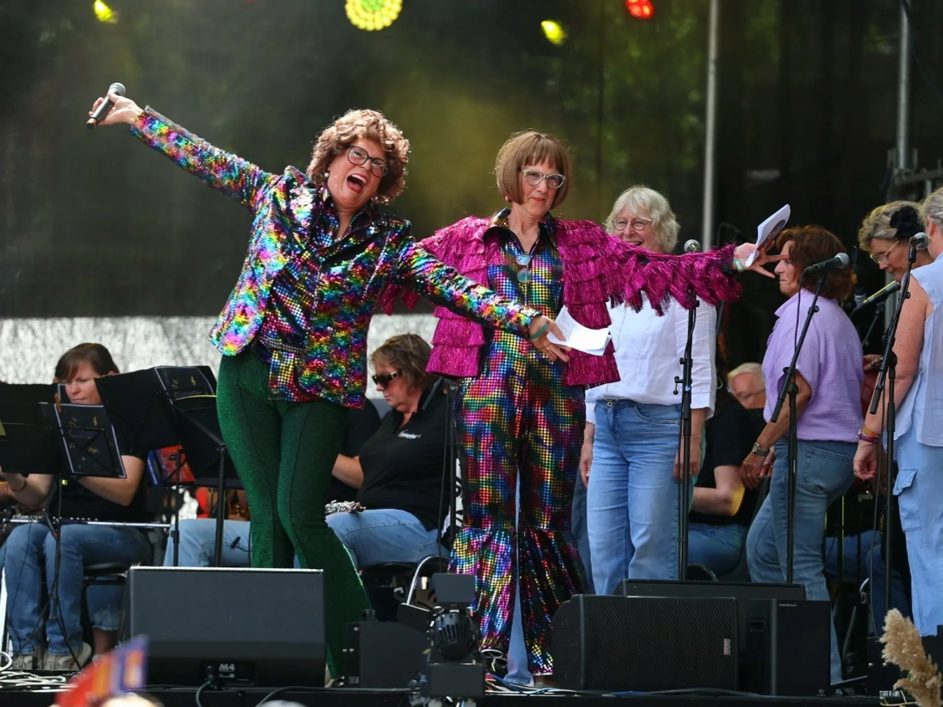 Twee mensen in kleurrijke kostuums optreden op een podium tijdens een festival.