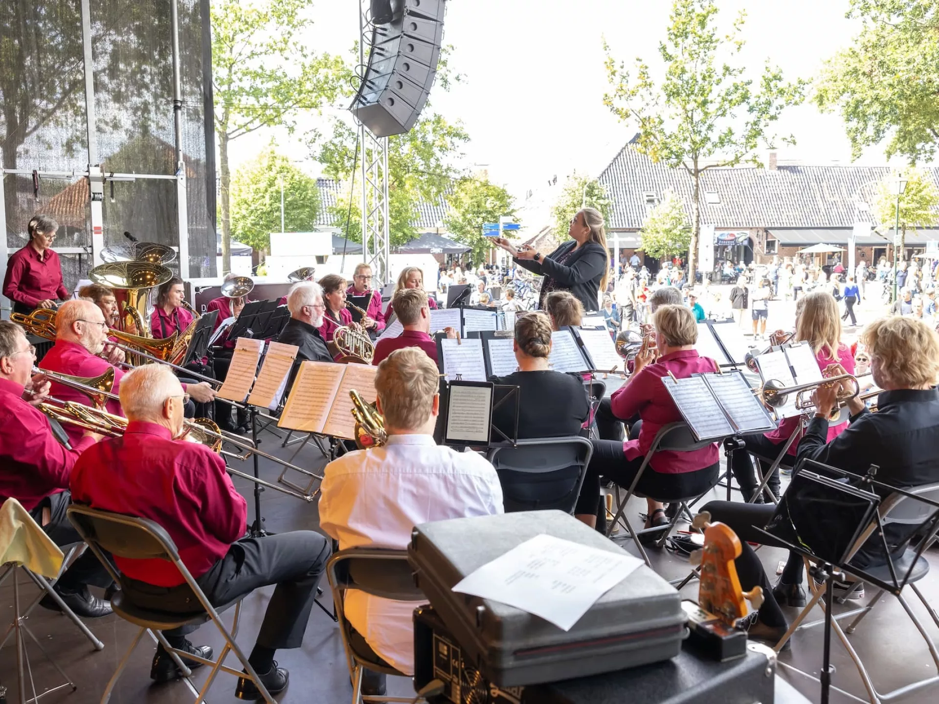 Je ziet een orkest vanaf het podium op een zonnige dag. In de verte zie je het publiek kijken.
