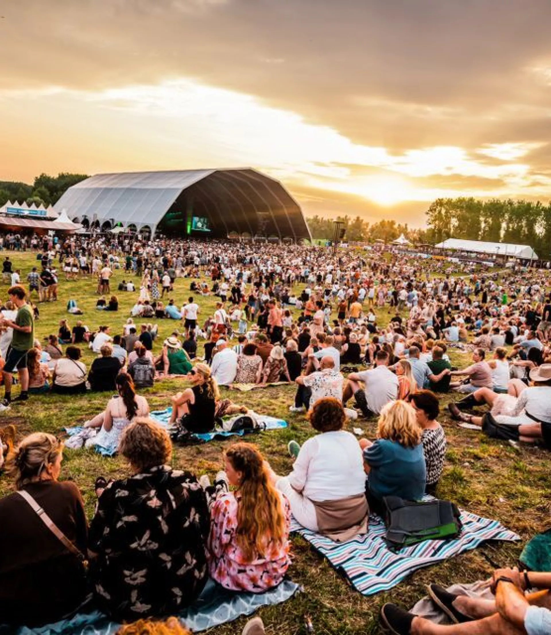 Buitenfestival bij zonsondergang met grote menigte.