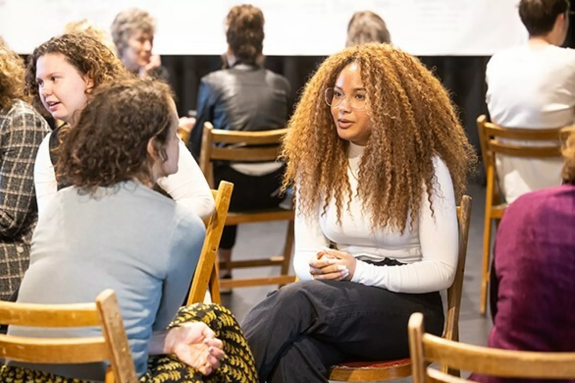 De Onmisbare Schakel - Drenthe - Twee mensen praten met elkaar. Ze zitten in een zaal waar mensen een workshop aan het volgen zijn.