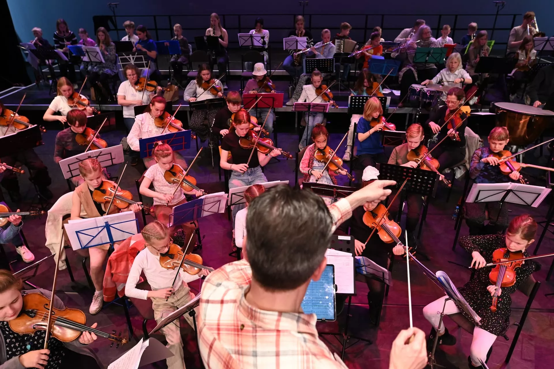 Kinderorkestleden spelen viool onder leiding van de dirigent.
