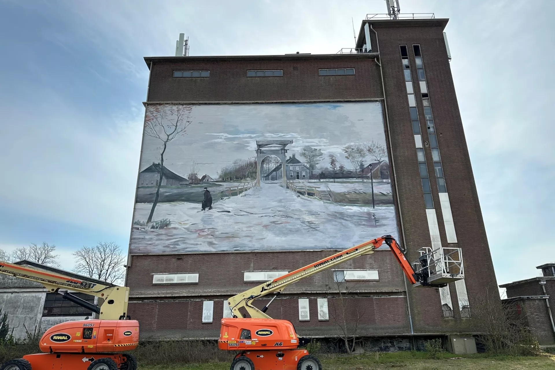 Muurschildering van een winterlandschap op een gebouw met twee hoogwerkers ervoor.
