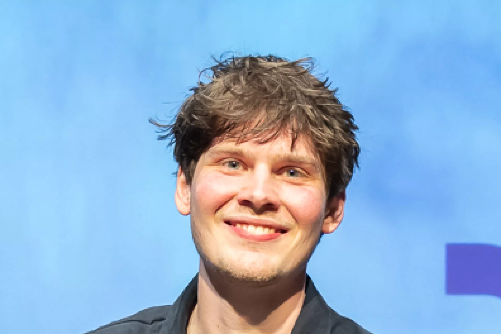 Winnaar Micha poseert met cheque van €2.500, sculptuur en bloemen op het podium.