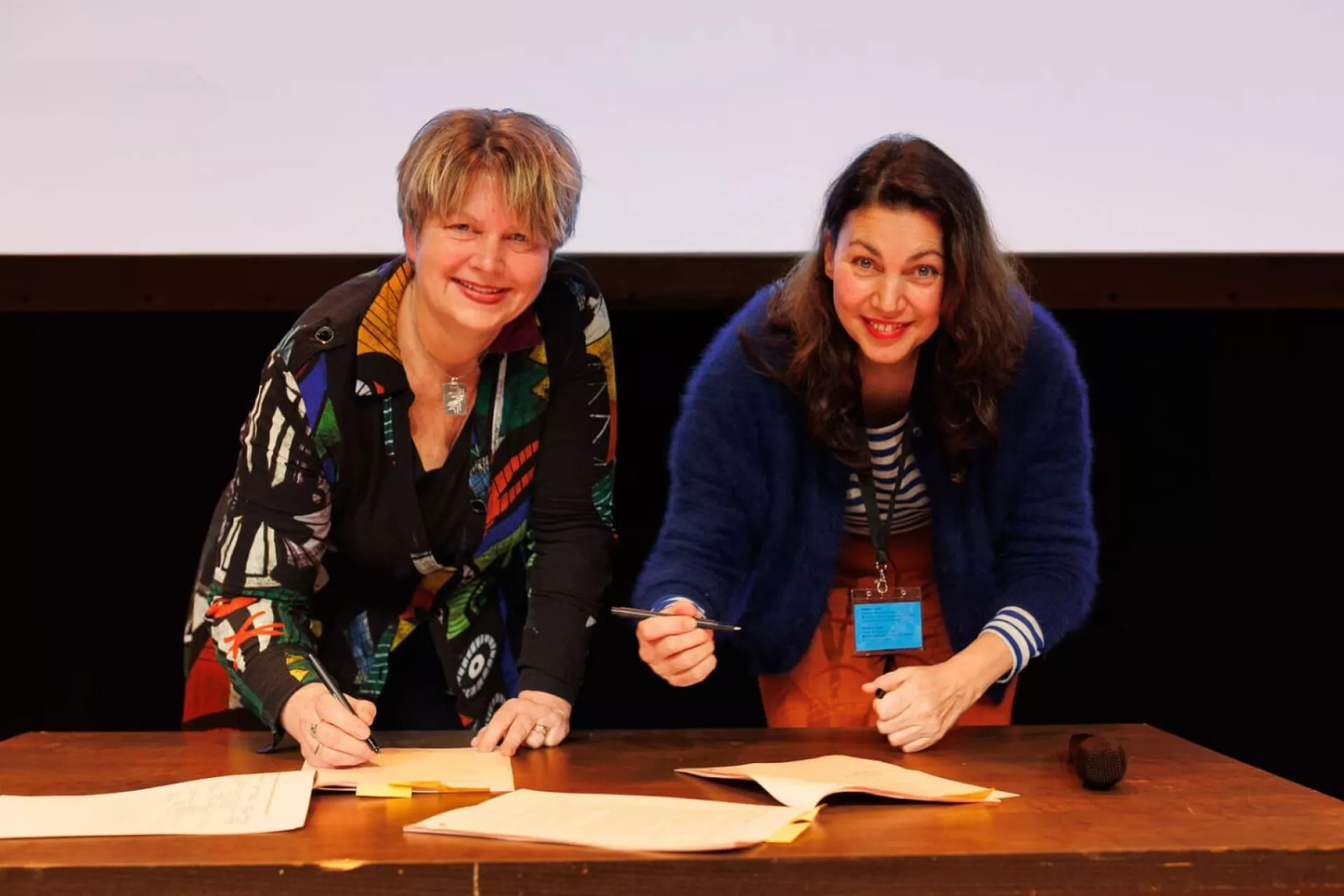 Twee vrouwen die documenten ondertekenen aan een tafel.