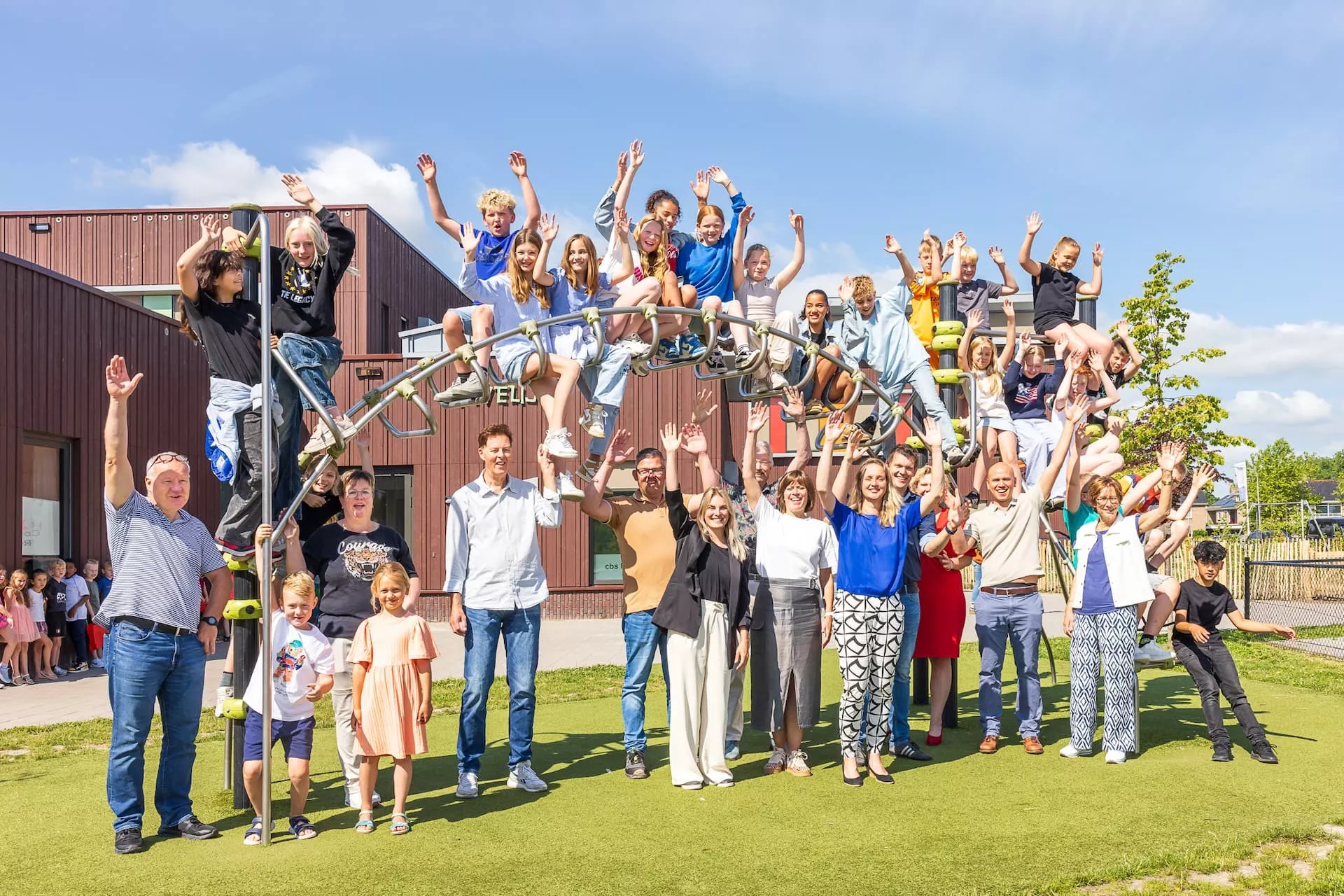 Juichende kinderen en leerkrachten rond een klimtoestel op het schoolplein.