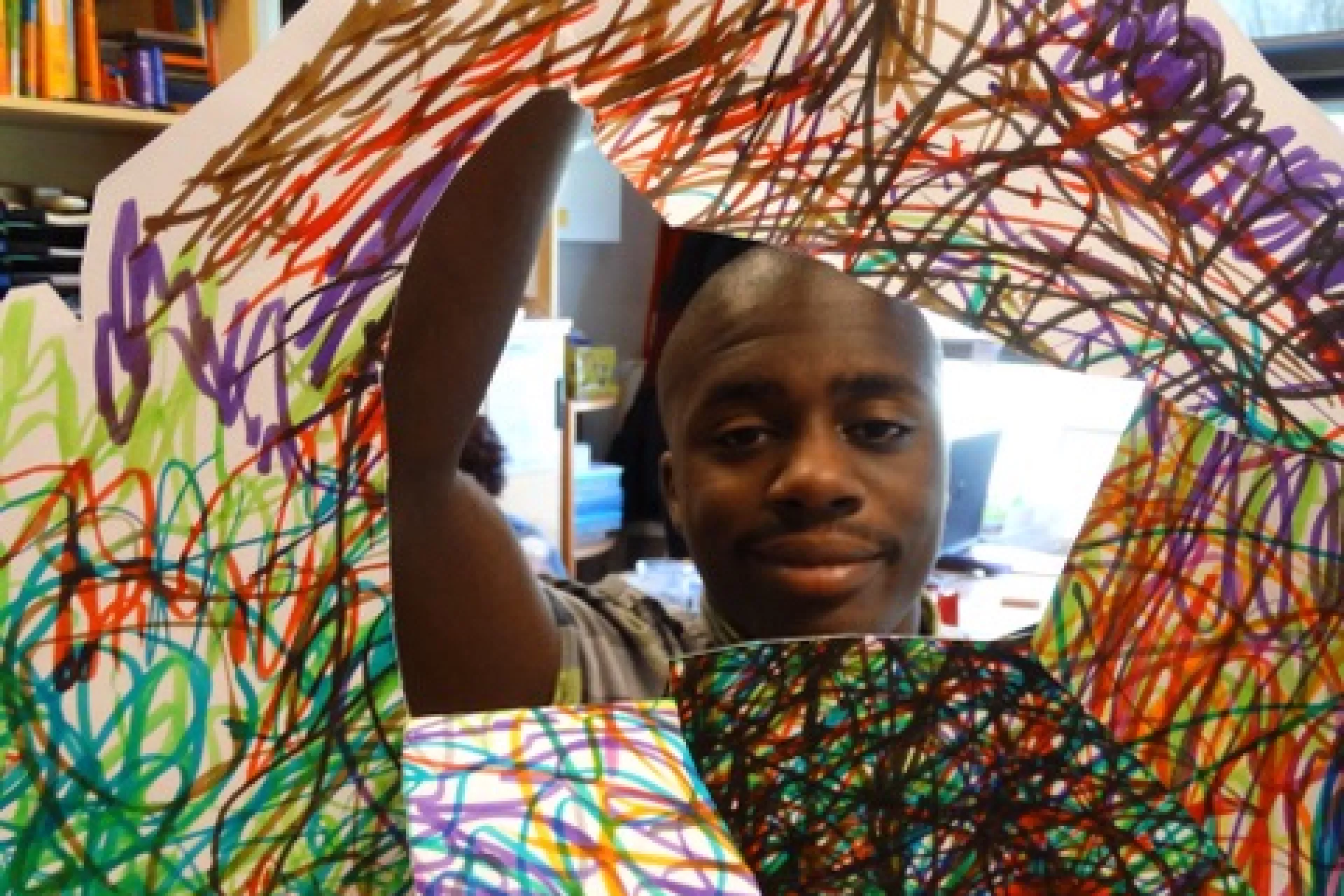 Een jongen toont een kleurrijk kunstwerk met krabbels.